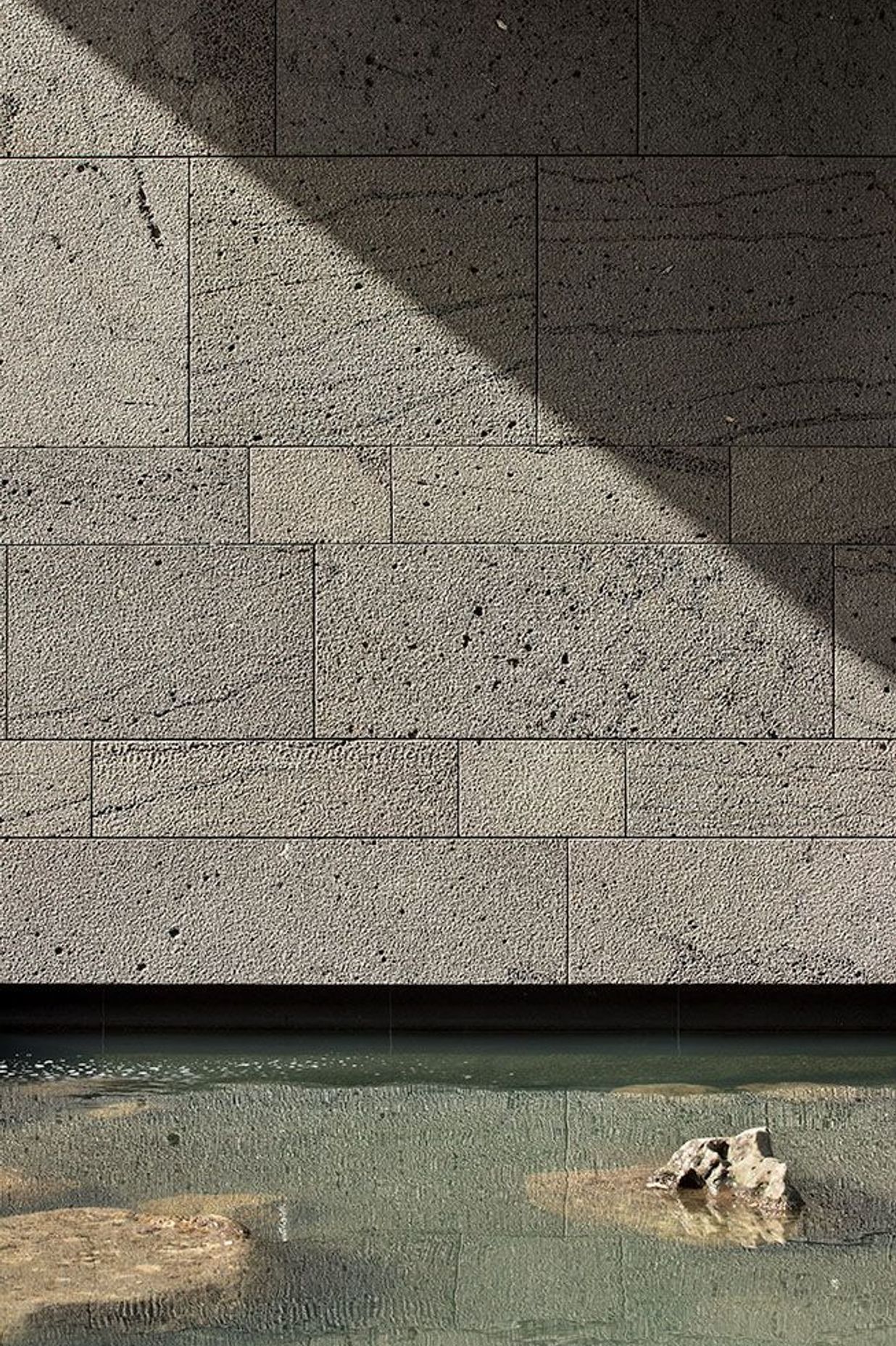 A 'bird-pecked' blue basalt stone wall is reflected in one of the reflection pools.