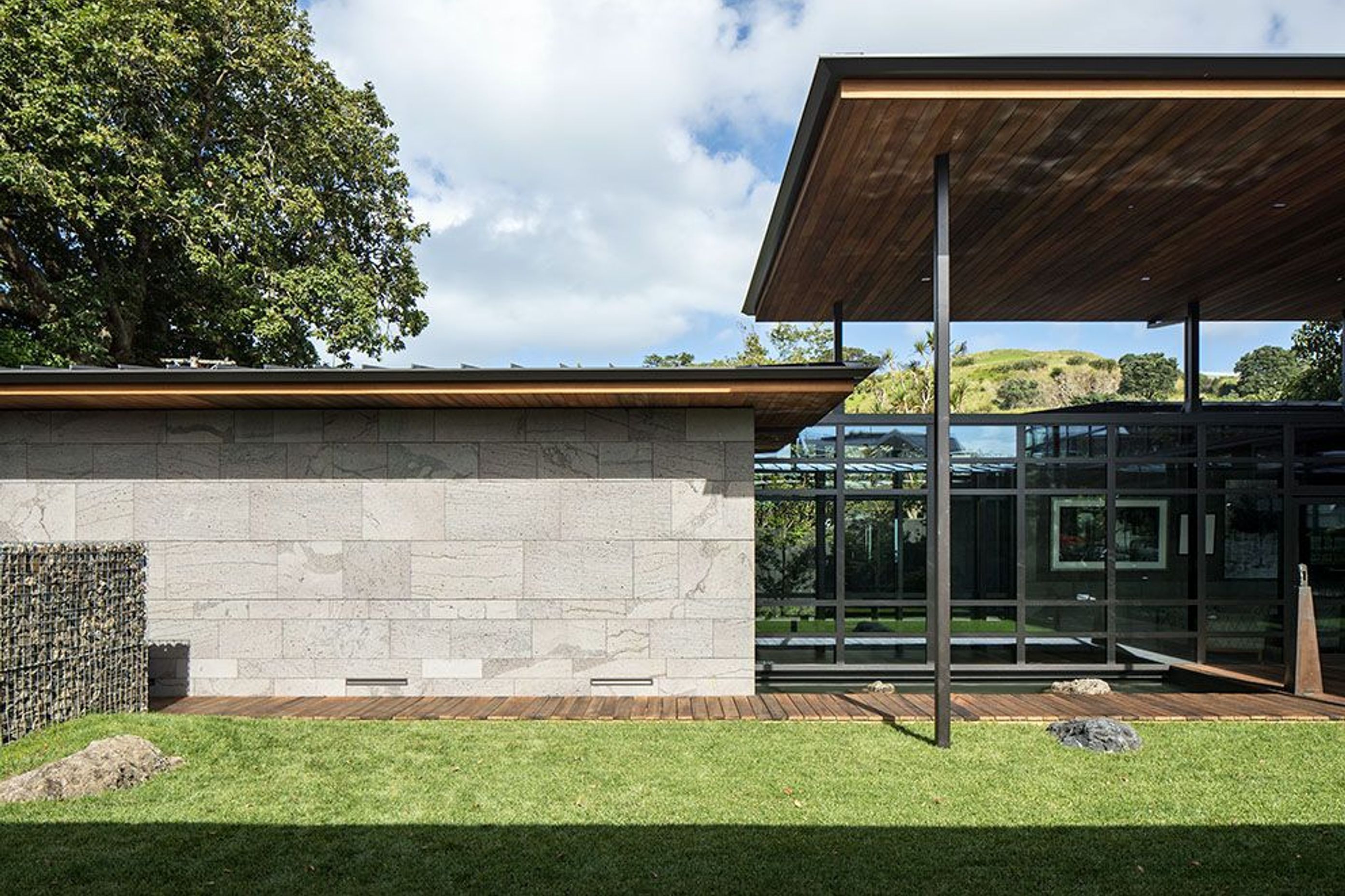 Local mountain Maungauika can be seen under the roof overhang from the outdoor room. The main entry (left) is lined by the bluestone-clad garage and the stone gubeon wall.
