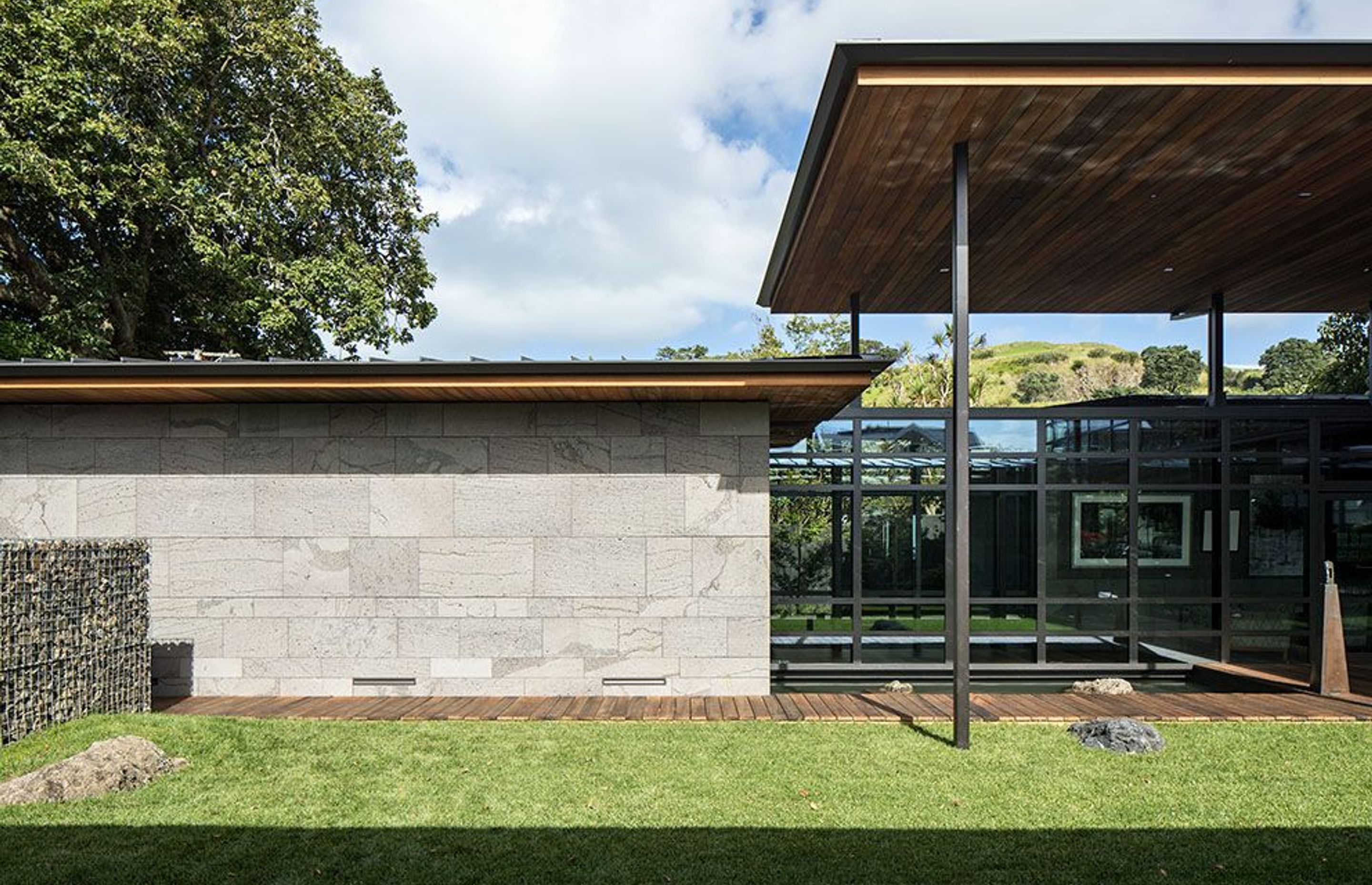 Local mountain Maungauika can be seen under the roof overhang from the outdoor room. The main entry (left) is lined by the bluestone-clad garage and the stone gubeon wall.