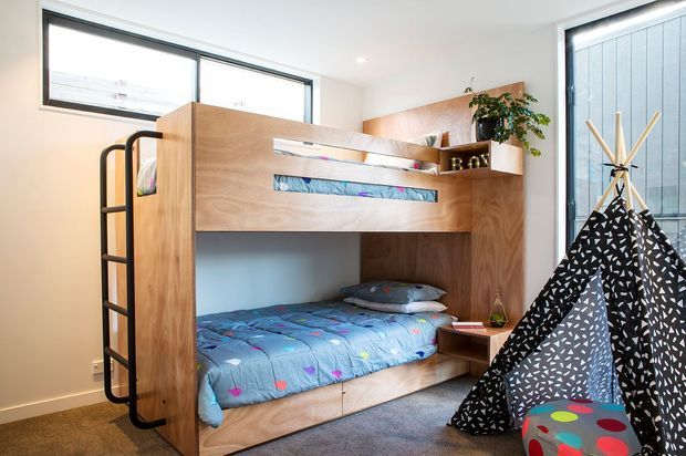 Bright children's bedroom featuring a built-in timber bunk bed with integrated ladder, shelving and drawers, colourful bedding, and a black-and-white patterned teepee tent. Large windows provide abundant natural light, while grey carpet and white walls create a clean backdrop.