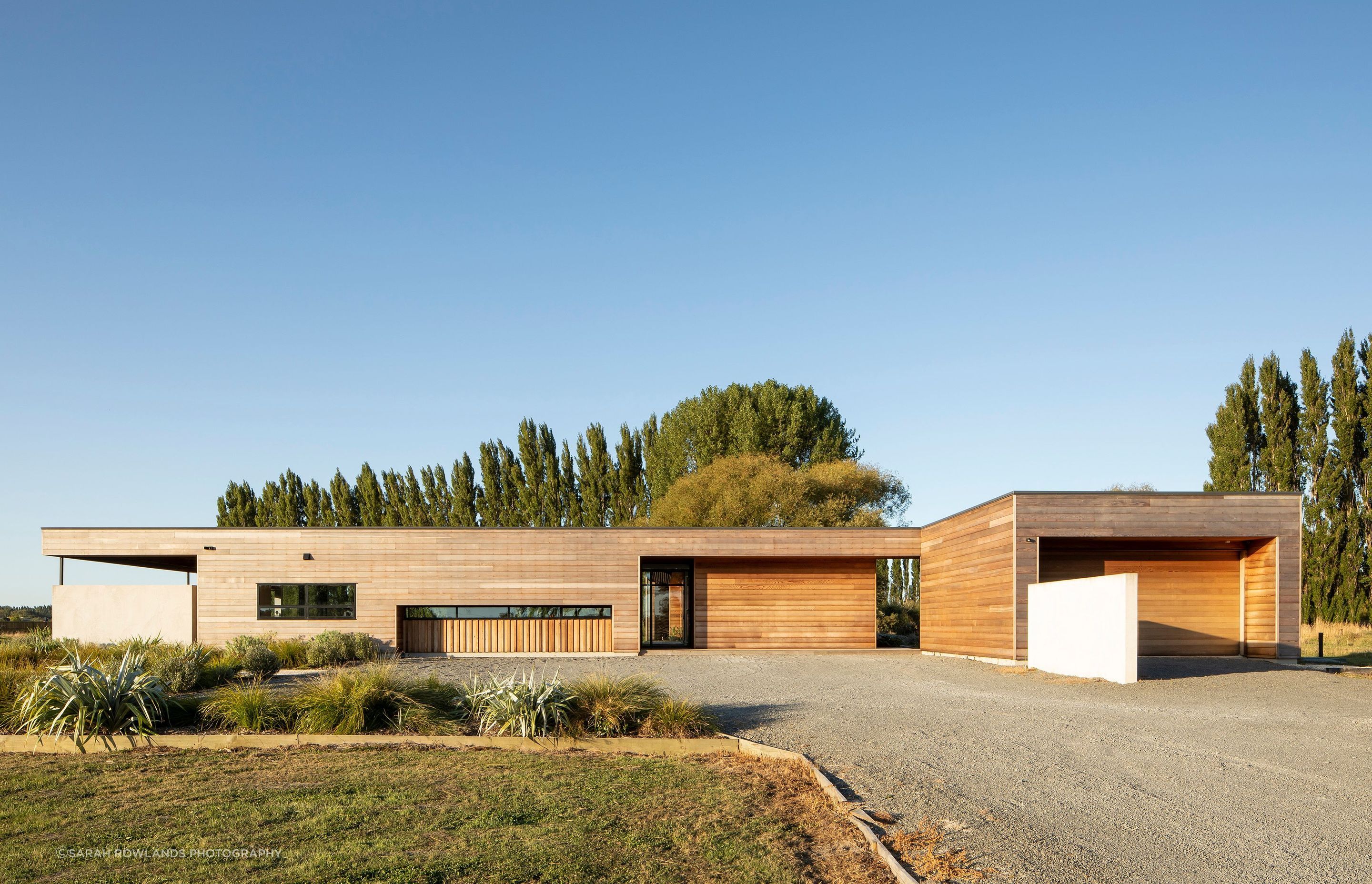 Clad in horizontal cedar, the south-west elevation features an outdoor room on the left, the entrance/porch in the middle and the garage to the right, with a turning circle out front.
