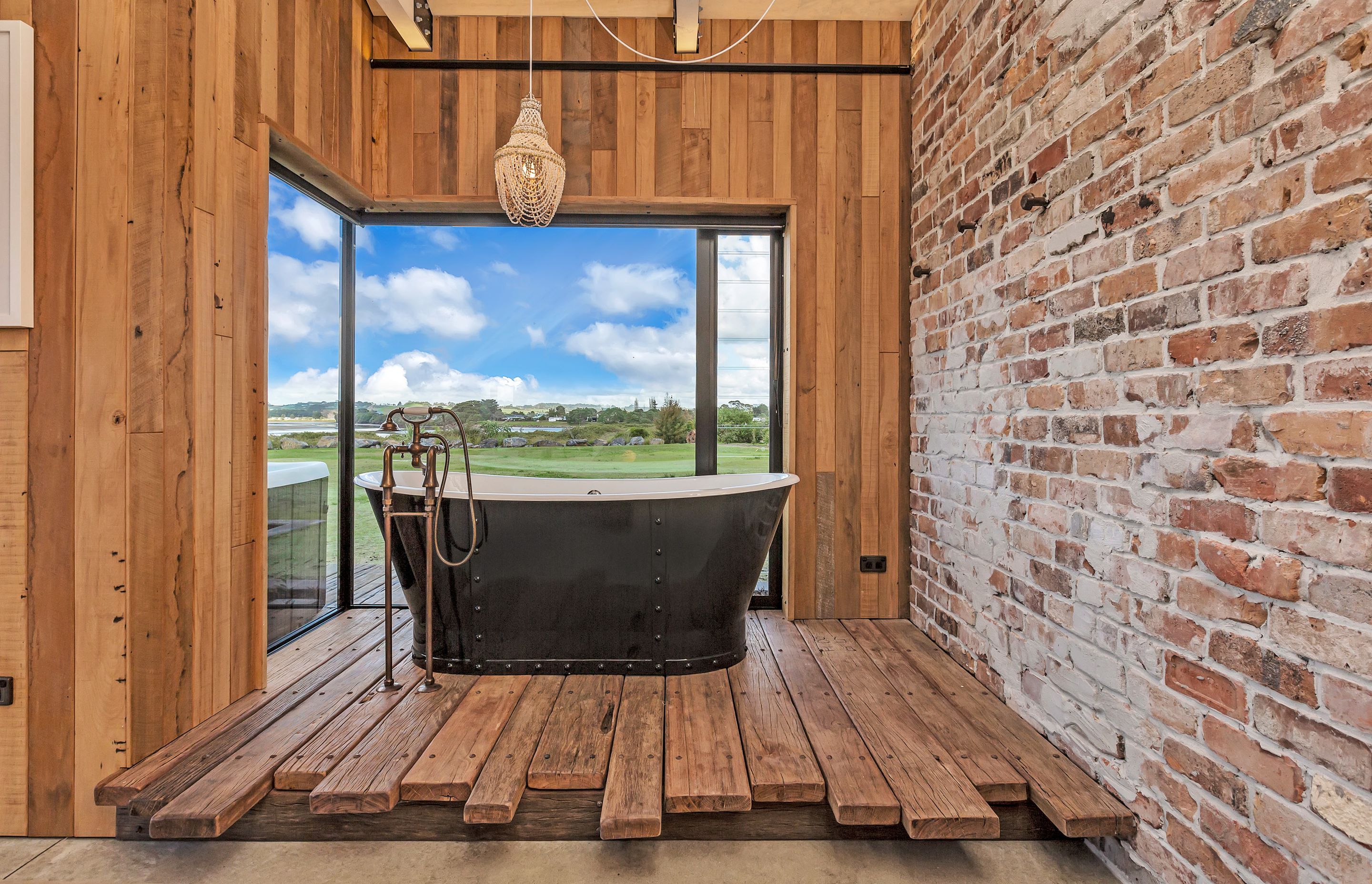 The bath sits on a handcrafted timber platform and features recycled brass exposed pipework and tapware.