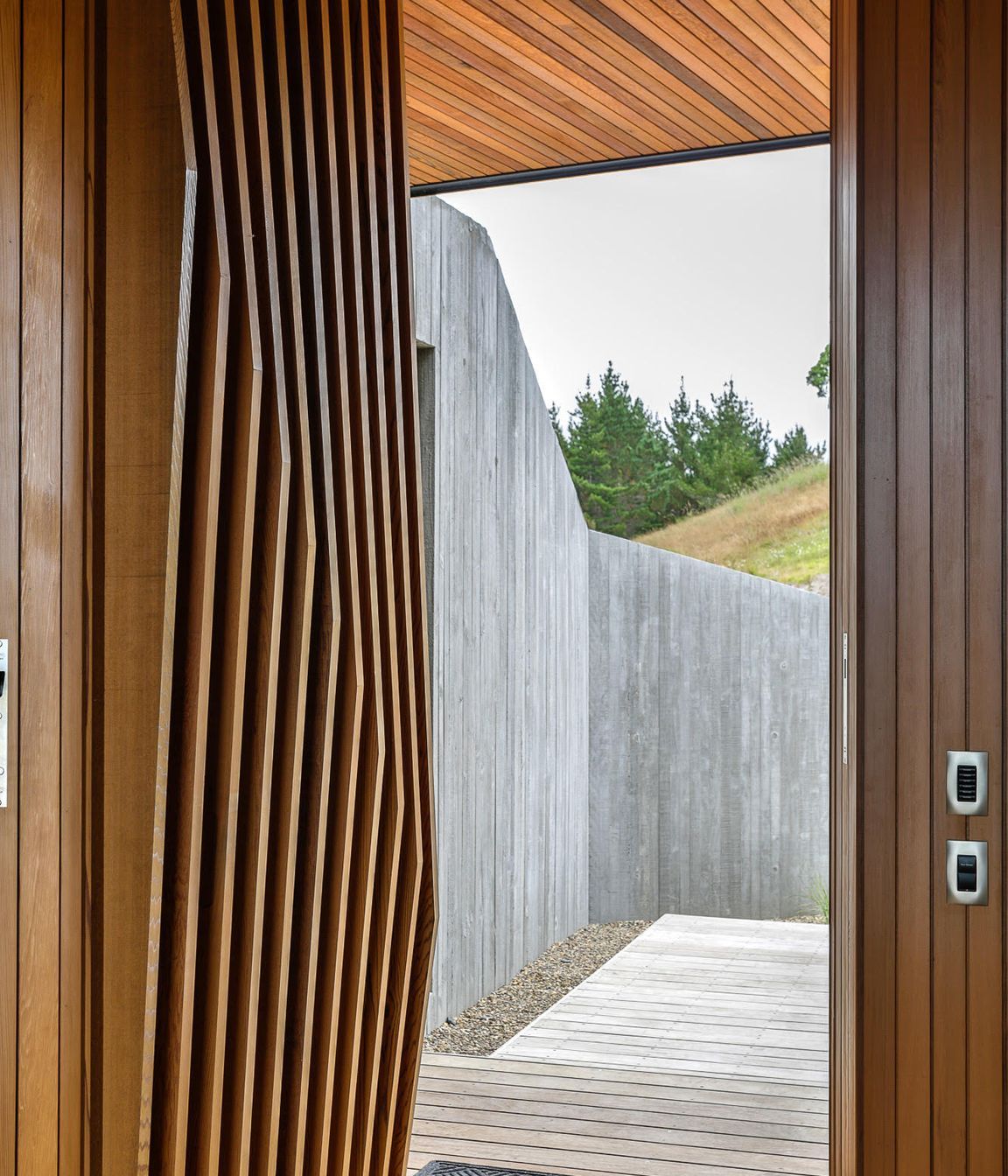 The faceted cedar fins on the main entry door each have a slighty different angle, playing on the vertical in situ formwork pattern of the spine entry wall.