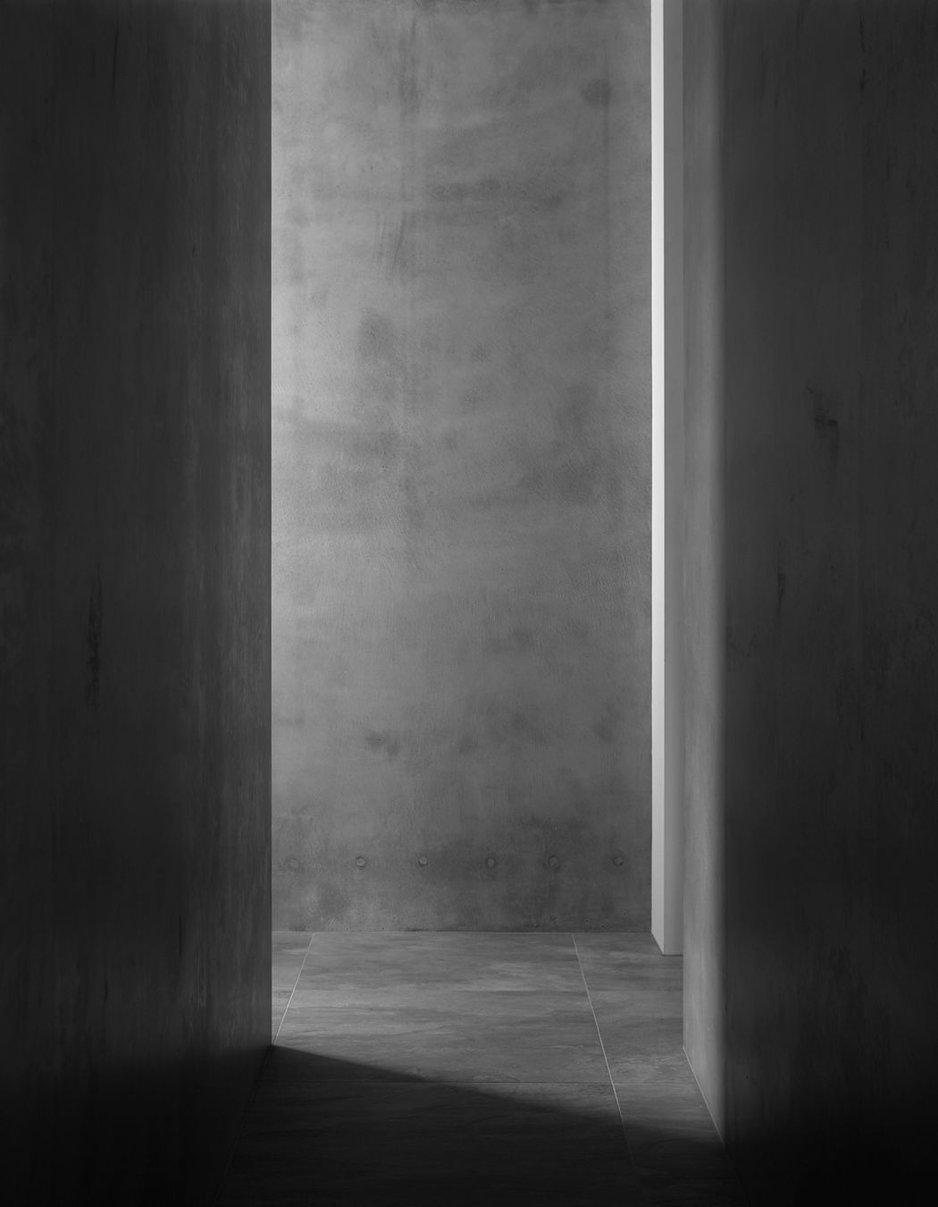 Grey concrete walls and tiled stone flooring creates a serene textural corridor space.