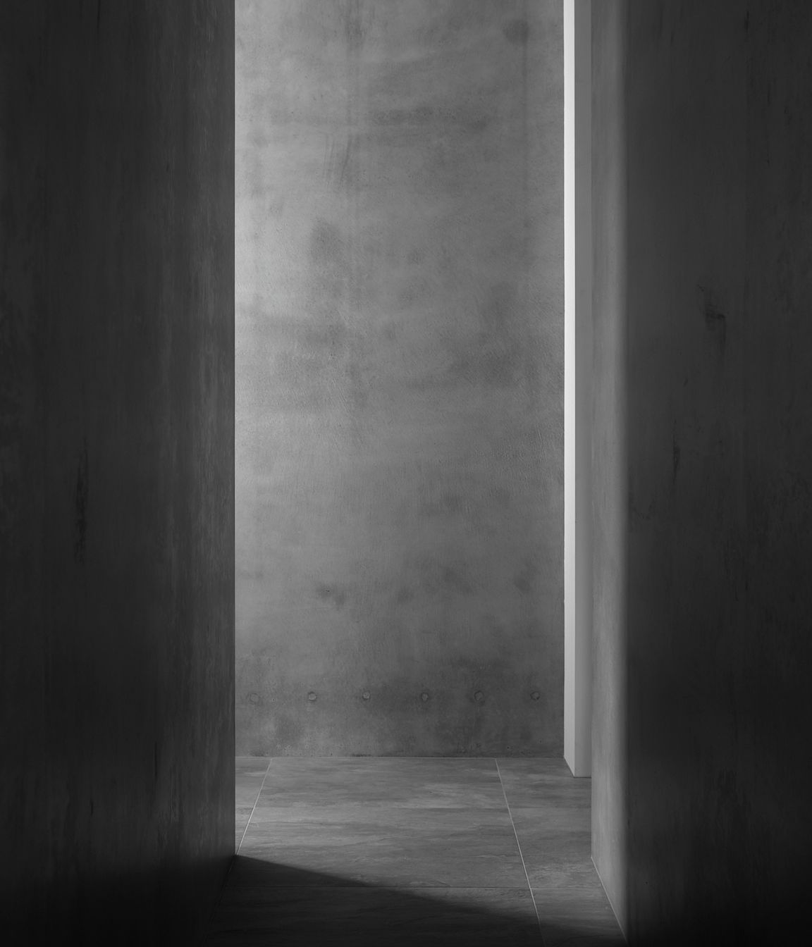 Grey concrete walls and tiled stone flooring creates a serene textural corridor space.