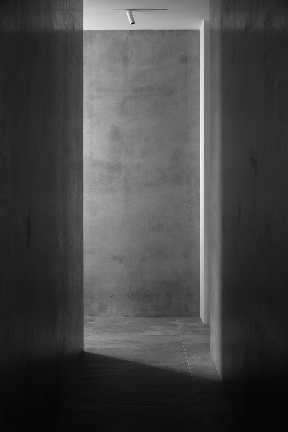 Grey concrete walls and tiled stone flooring creates a serene textural corridor space.