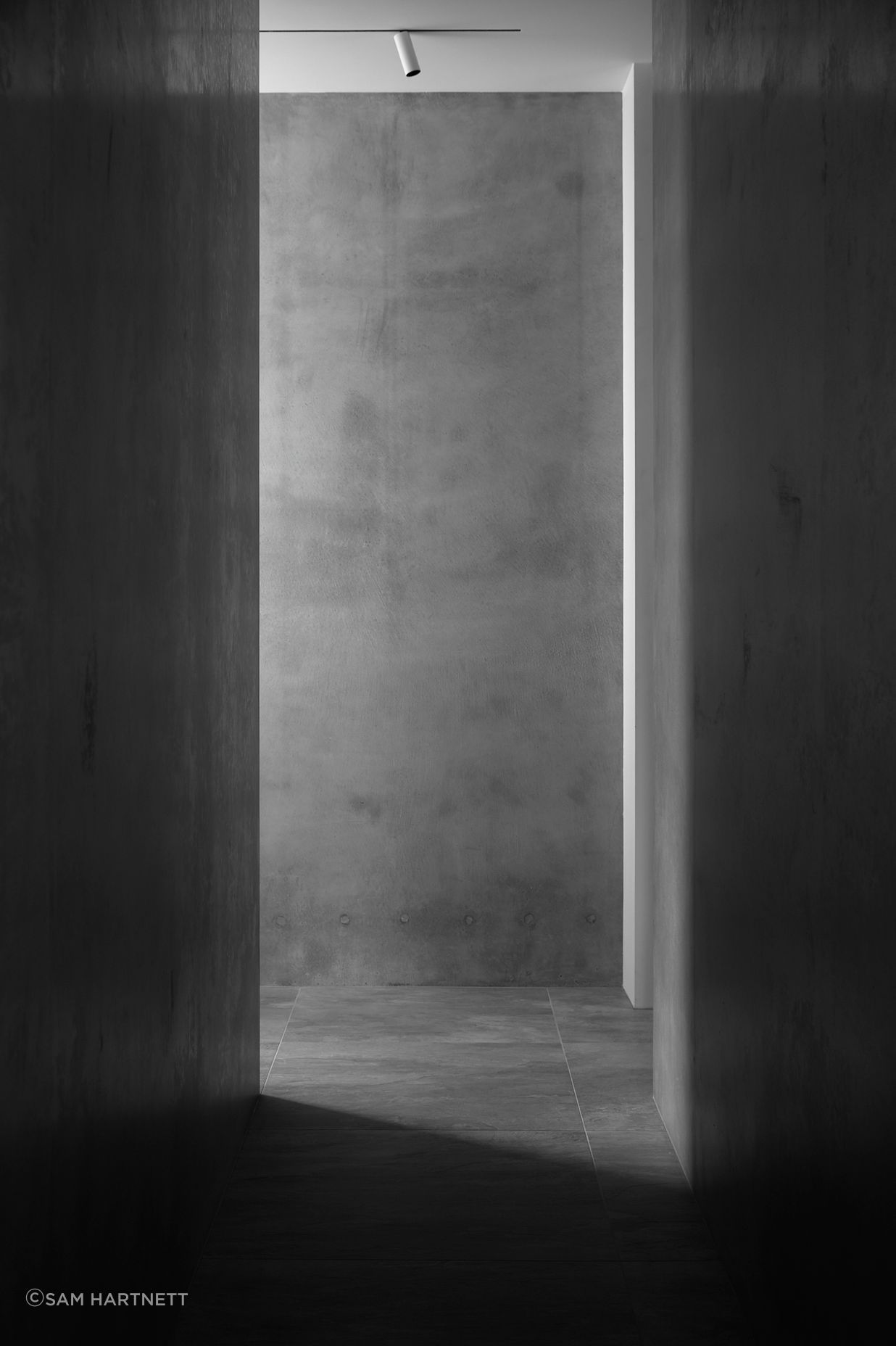 Grey concrete walls and tiled stone flooring creates a serene textural corridor space.