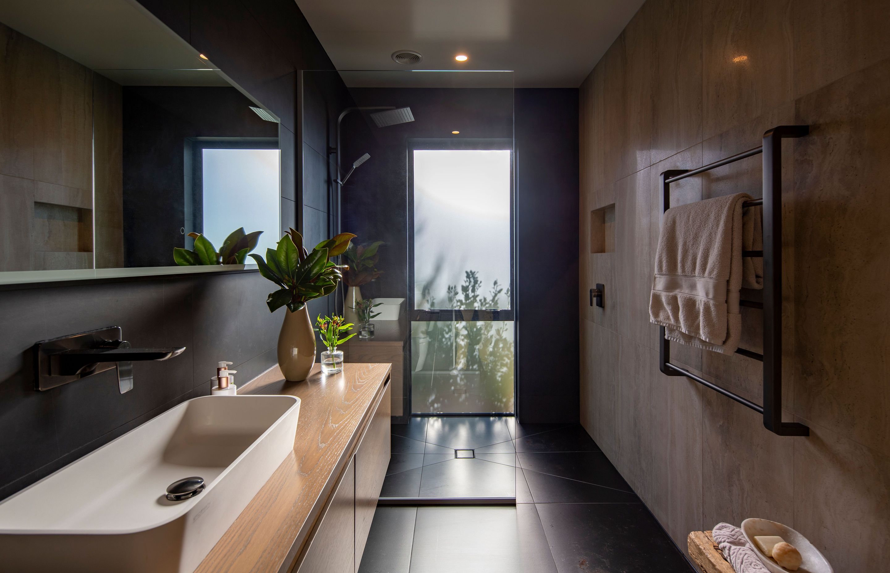 Dark tiling and a walk-in shower feature in the main bathroom.