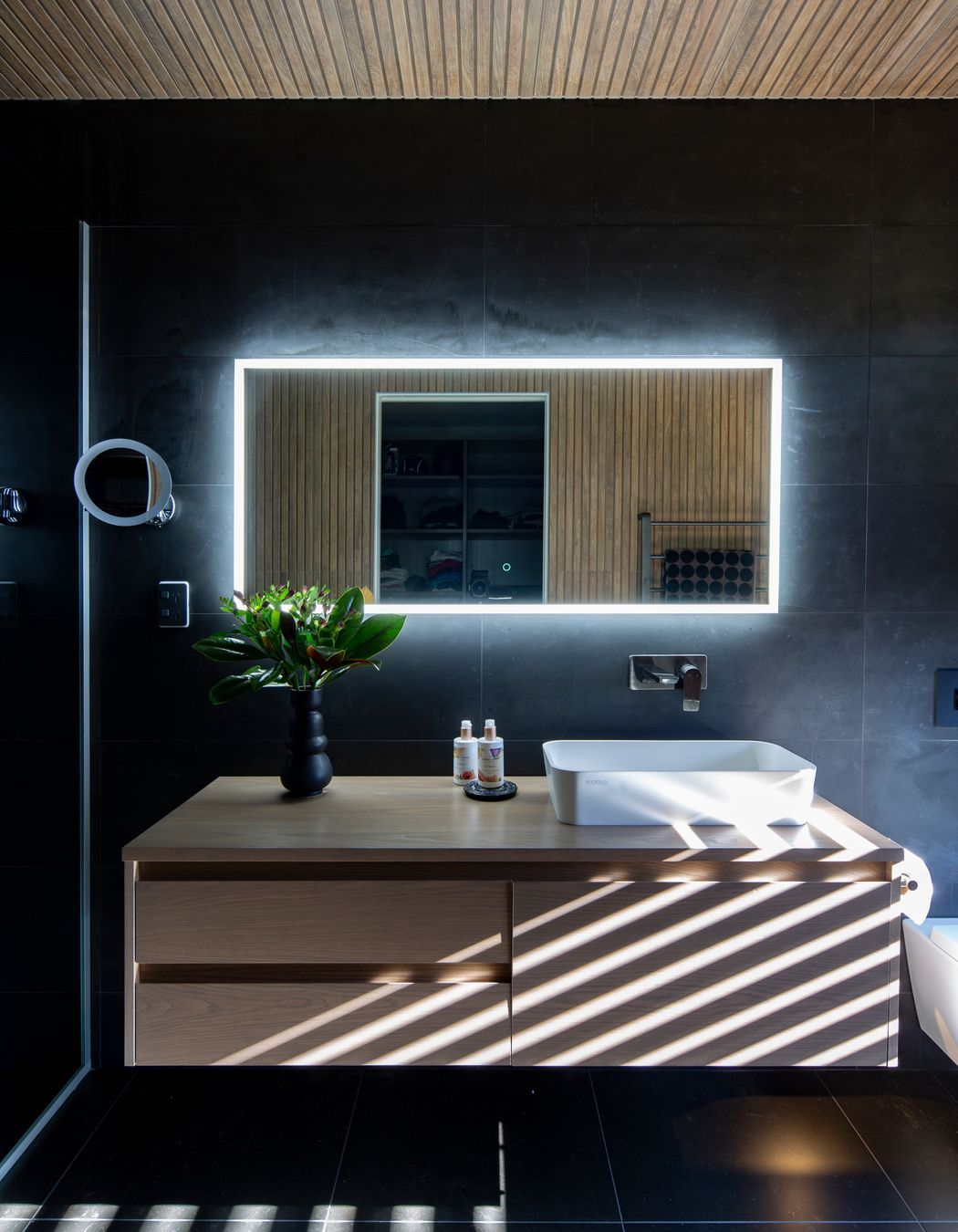 Wood-look ceiling tiles in the ensuite and a wall-hung Sirocco Syrtari cabinet in 'Rural Oak' offset the moodiness of the floor-to-ceiling charcoal-toned wall tiles.