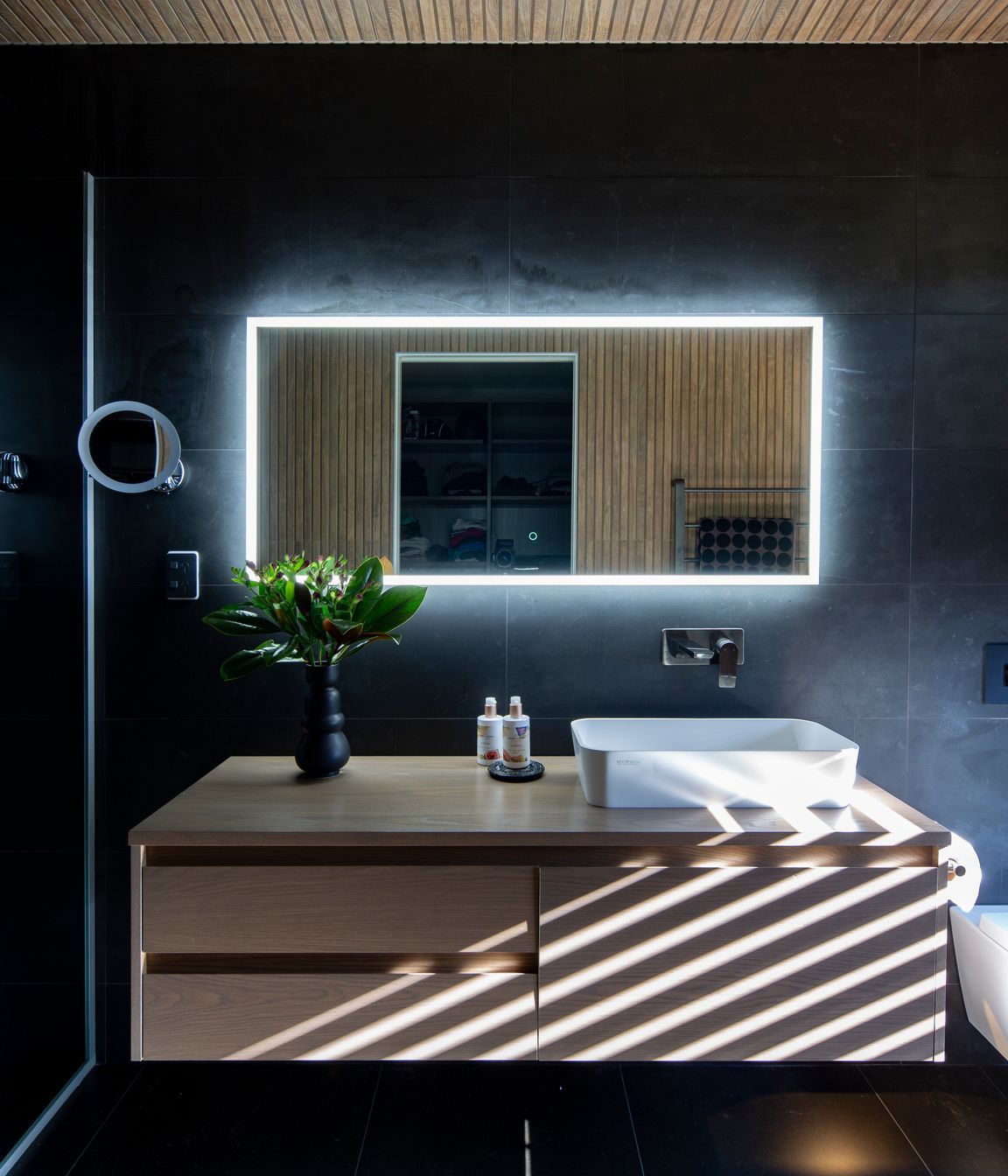 Wood-look ceiling tiles in the ensuite and a wall-hung Sirocco Syrtari cabinet in 'Rural Oak' offset the moodiness of the floor-to-ceiling charcoal-toned wall tiles.
