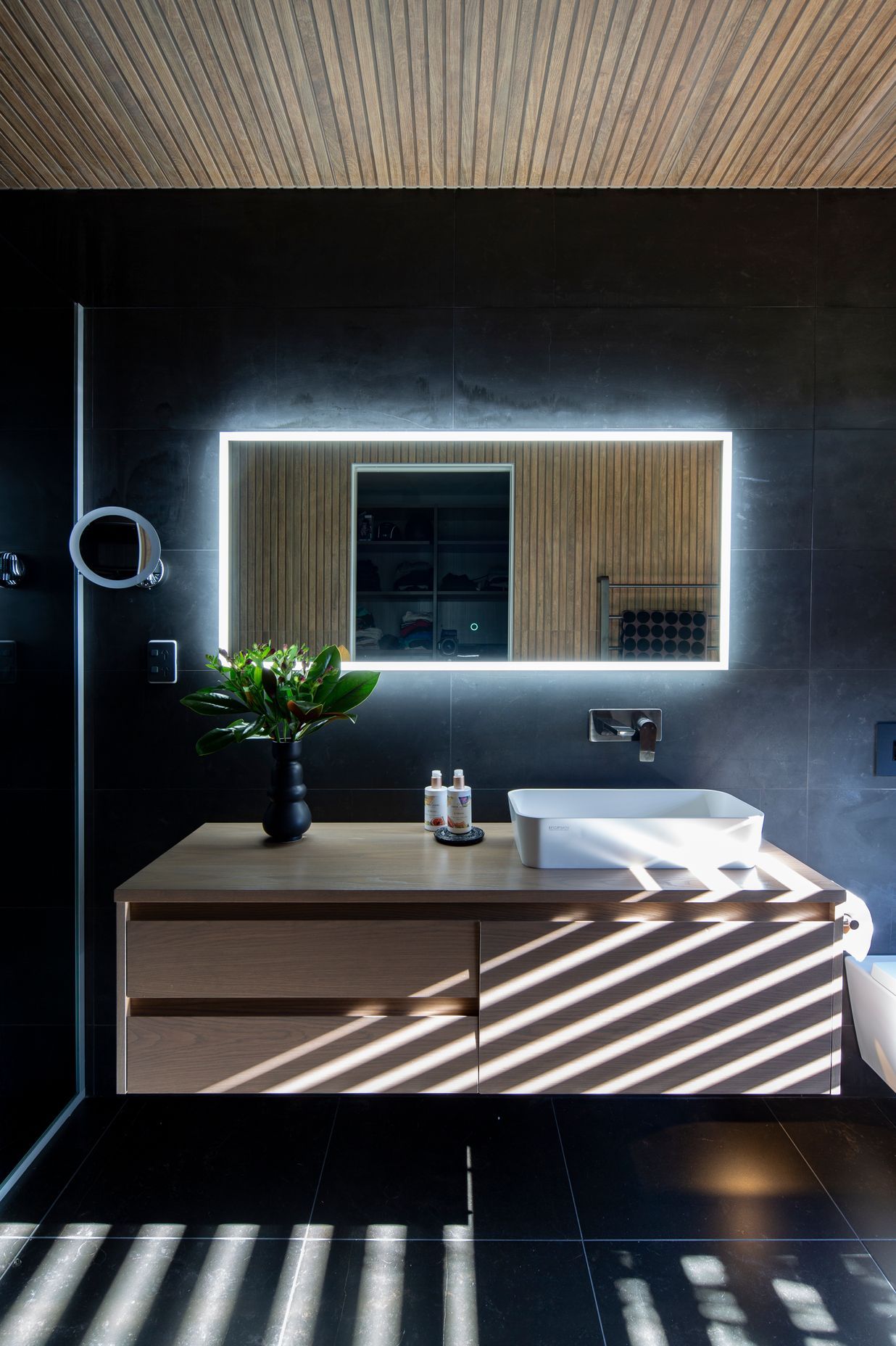 Wood-look ceiling tiles in the ensuite and a wall-hung Sirocco Syrtari cabinet in 'Rural Oak' offset the moodiness of the floor-to-ceiling charcoal-toned wall tiles.