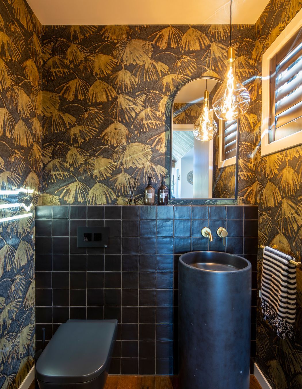 The powder room is furnished with a striking Como concrete floor basin in 'Midnight' with a dash of decorativeness provided by the Iliad by Zoffany wallpaper. A Voronoi globe, by Tala, is reflected in the mirror.