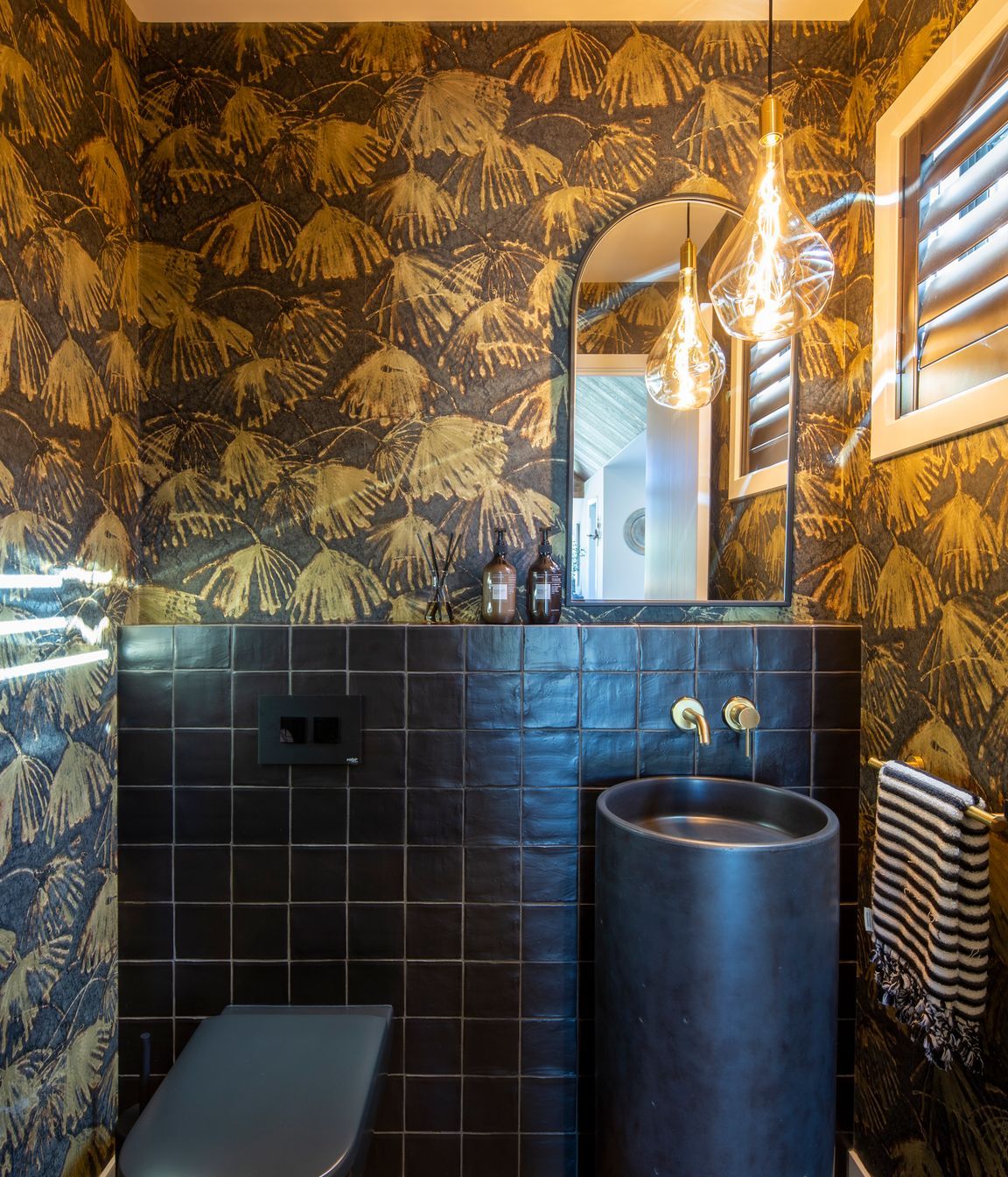 The powder room is furnished with a striking Como concrete floor basin in 'Midnight' with a dash of decorativeness provided by the Iliad by Zoffany wallpaper. A Voronoi globe, by Tala, is reflected in the mirror.