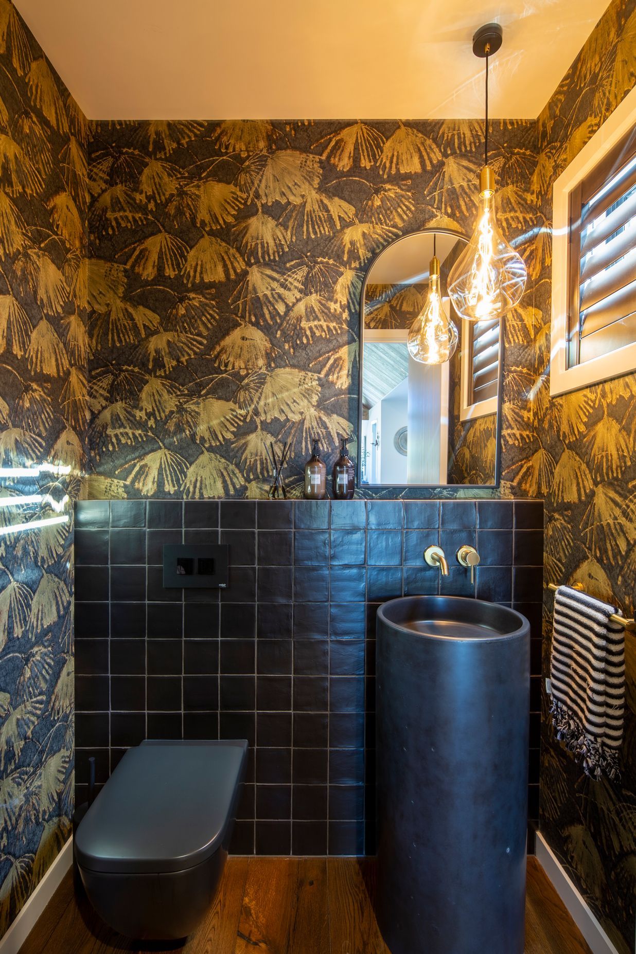 The powder room is furnished with a striking Como concrete floor basin in 'Midnight' with a dash of decorativeness provided by the Iliad by Zoffany wallpaper. A Voronoi globe, by Tala, is reflected in the mirror.