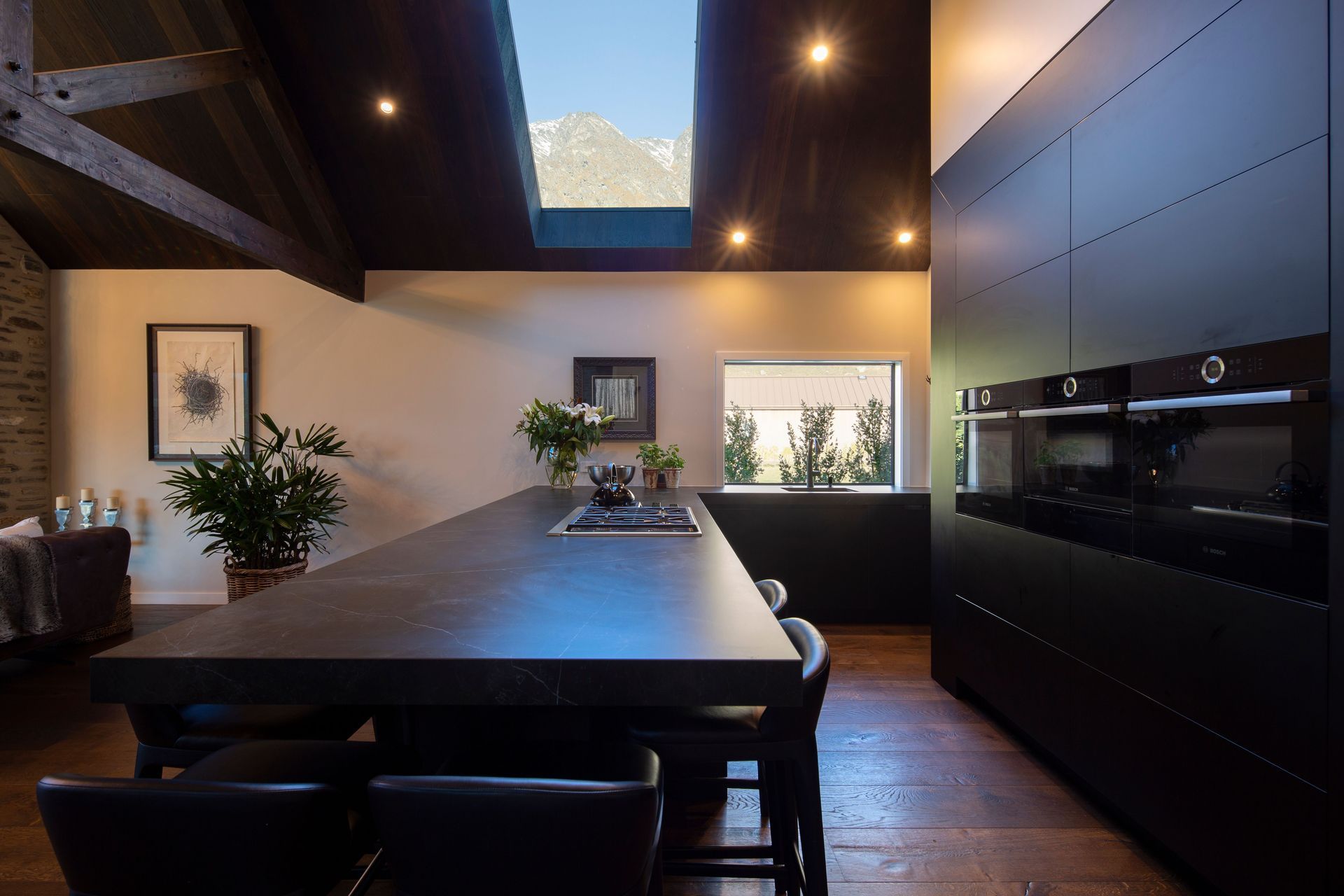 The kitchen features charcoal-toned cabinetry and a matte-black peninsula with a hob inset for meal preparation while chatting with friends. Through the skylight, the cook gets a peek at The Remarkables.