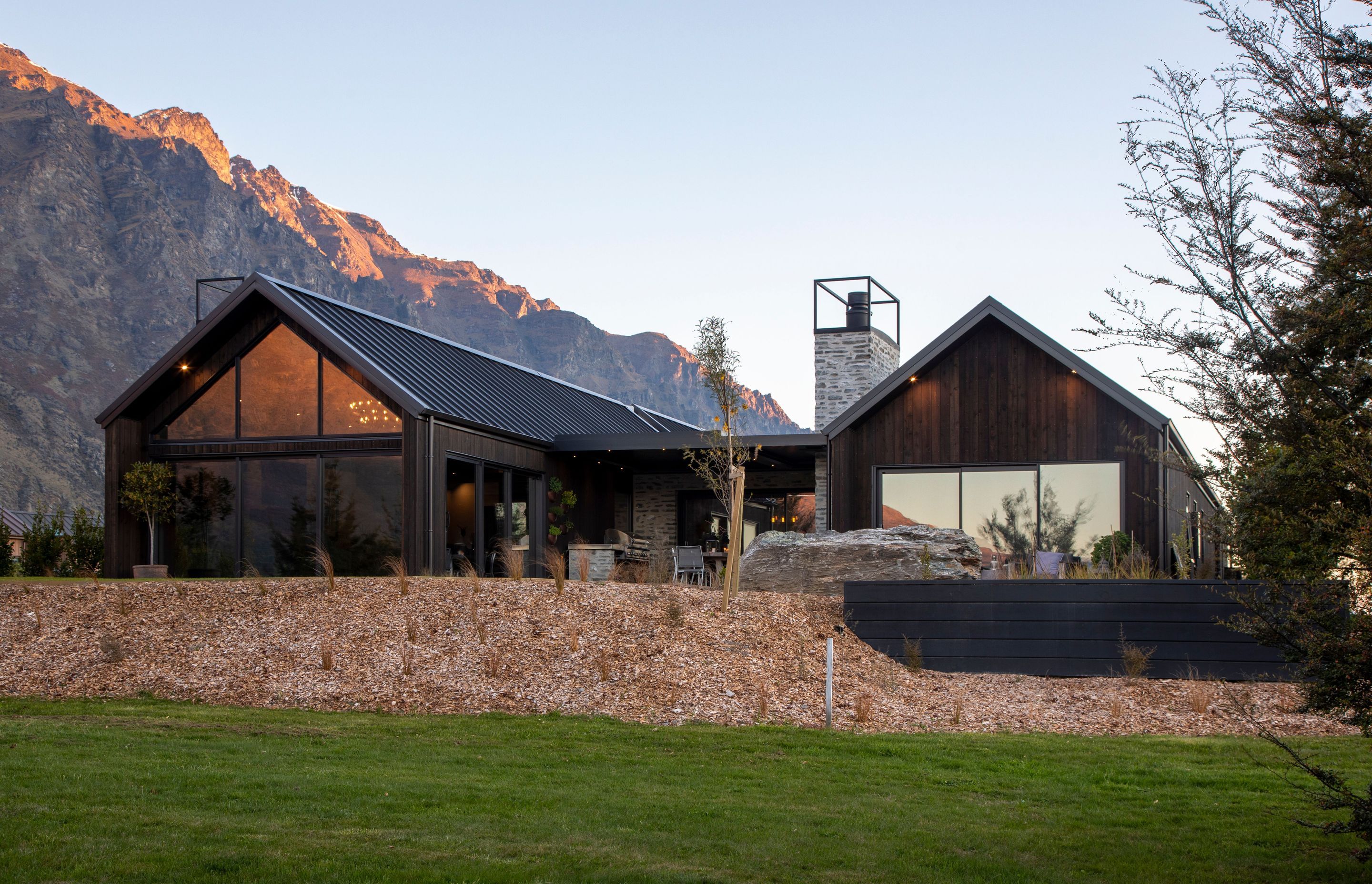 The twin gables and knotty vertical cedar cladding. stained in Dryden Woodoil 'Midnight', allow the home to blend with the typography and colours of the landscape.