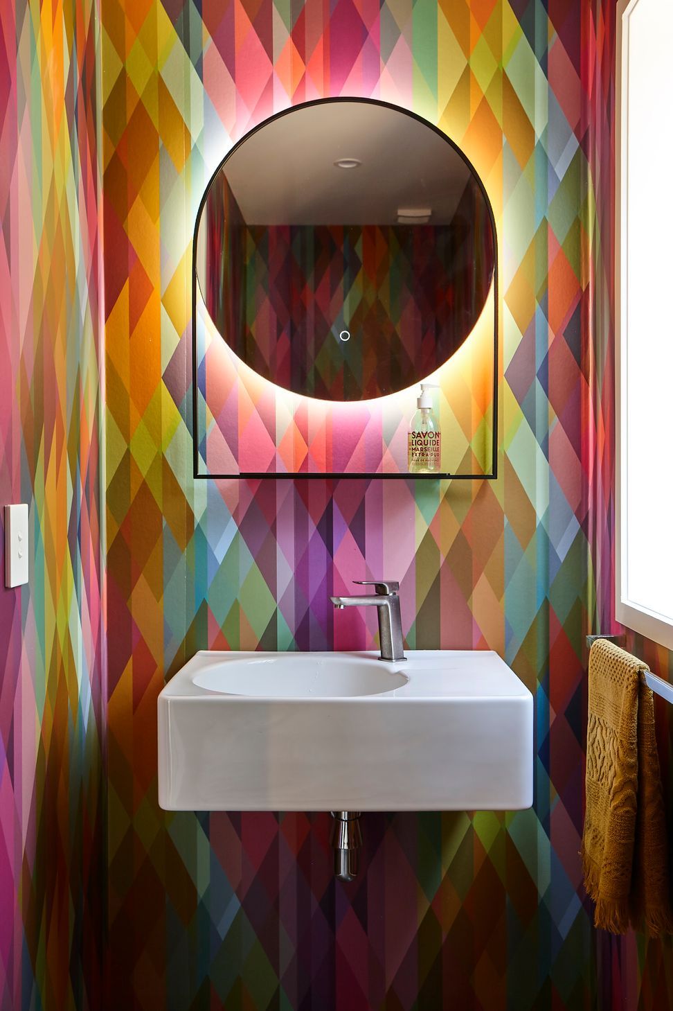 The powder room introduces a playful moment within the home, featuring Cole & Son Geometric II Prism wallpaper that adds colour, pattern and personality to the compact space.