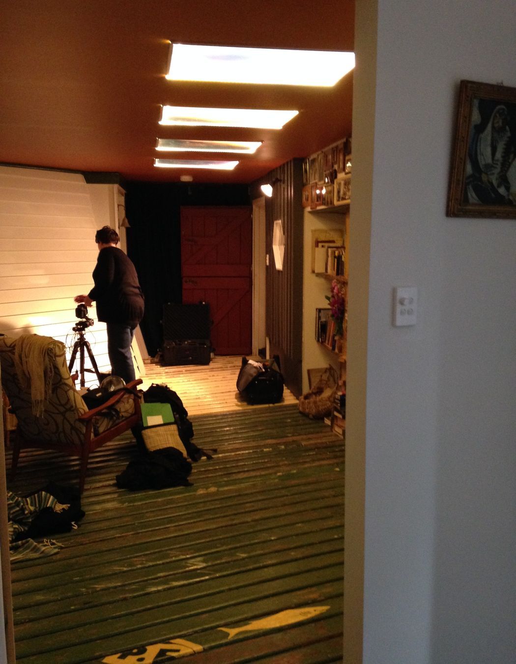 Connecting link space. Golden ceiling reflects the afternoon sun and warms the space. Custom perspex artworks are illuminated for ceiling lighting. Recycled weatherboard floor (not as hard as you would think). Bookcasing and other custom joinery made from Huon Pine reclaimed from crayfish holding tanks. Original wall of the windmill and bedroom shed seen towards the rear