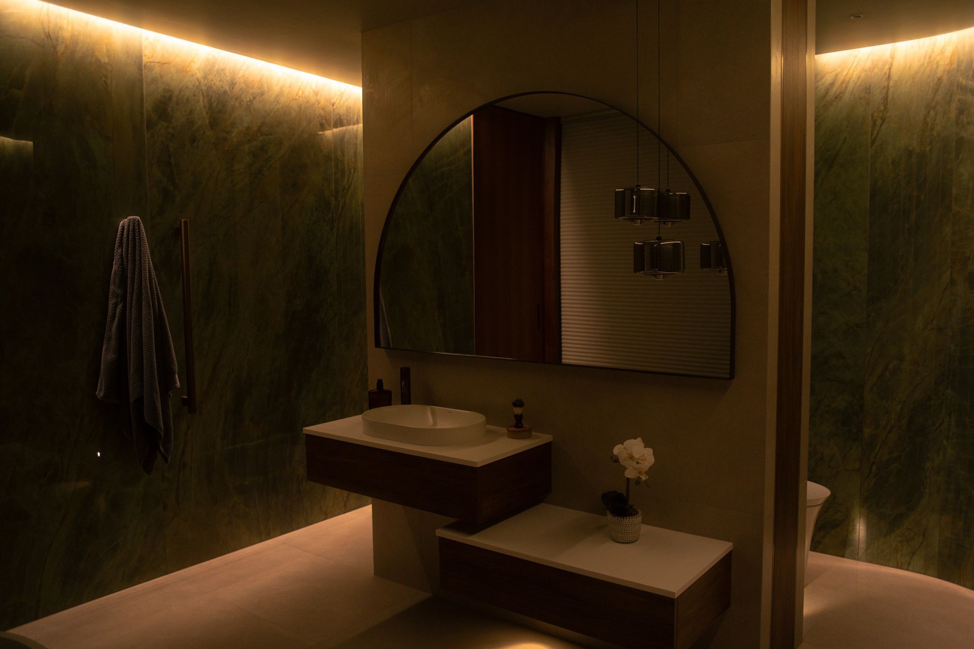 A carefully executed lighting detail that celebrates craftsmanship and form. Integrated LED strip lighting follows the curve of the bathroom wall, beautifully accentuating the natural texture and shape of the greenstone tiles while enhancing the architectural flow of the space.