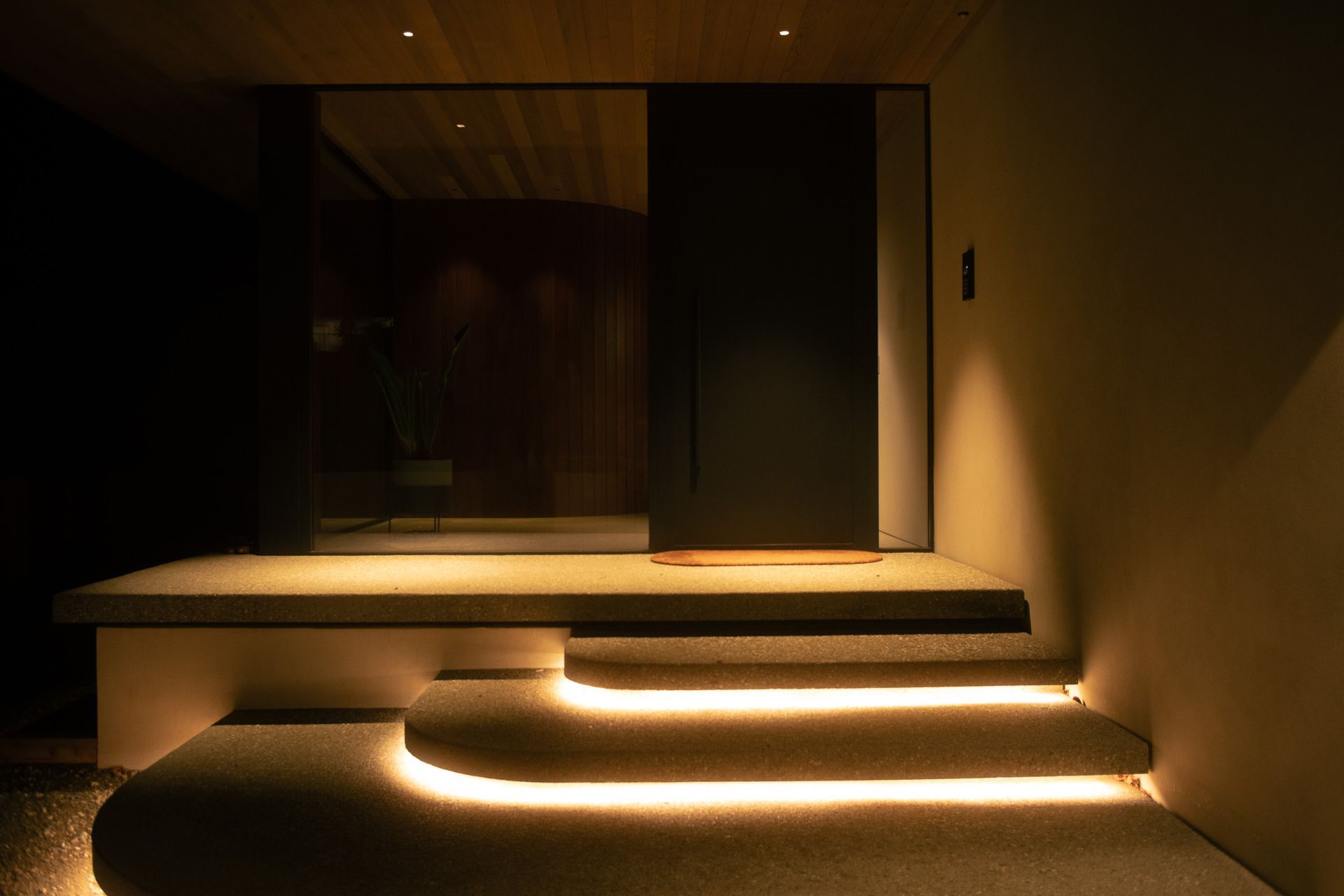 Extending the lighting experience beyond the interior, concealed LED strip lighting beneath the staircase creates a subtle floating effect, adding depth and drama to the exterior pathway. Complemented by Halcyon R534 Cevon Darklight Minis, the space is softly illuminated with precision and restraint.