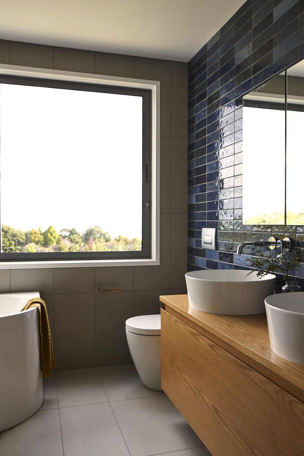 The ensuite combines rich blue wall tiles, grey floor tiles and bespoke oak cabinetry to create a calm, contemporary retreat. A framed view towards the ocean reinforces the home's strong connection to the surrounding landscape.