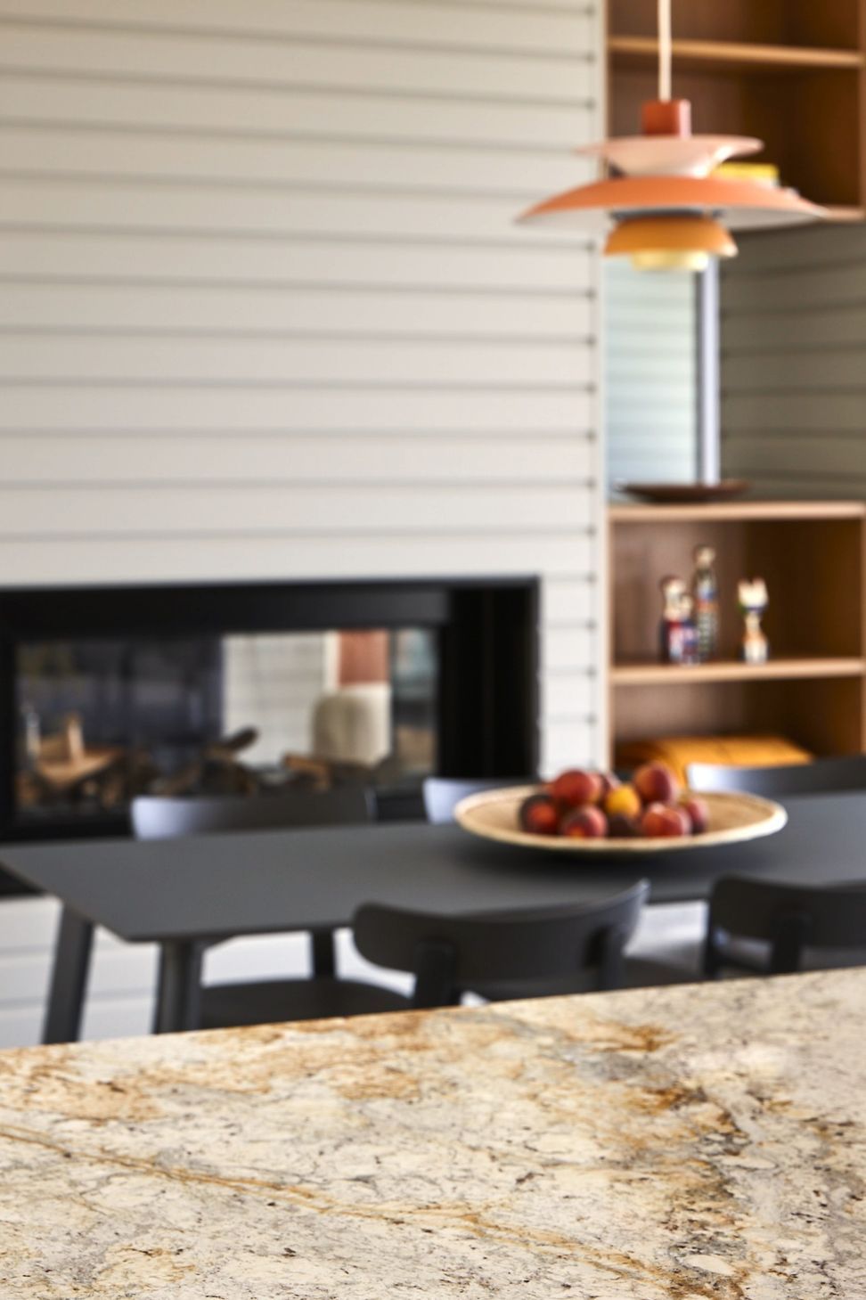 The kitchen centres around a beautifully crafted granite island, paired with warm oak cabinetry and a granite splashback. Above the dining table, an iconic orange Louis Poulsen PH5 pendant introduces colour and personality to the restrained interior palette.