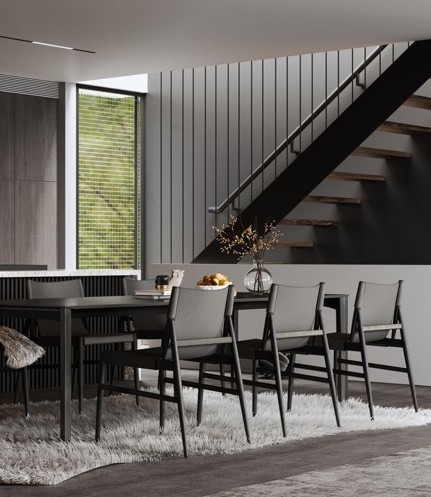A sophisticated dining area beneath an open staircase, featuring a long dark dining table with upholstered chairs, a textured grey rug, dark vertical wall panelling, a tall window with horizontal blinds, and a black steel stair structure with timber treads. The restrained monochromatic palette and clean geometric lines create a refined contemporary interior.