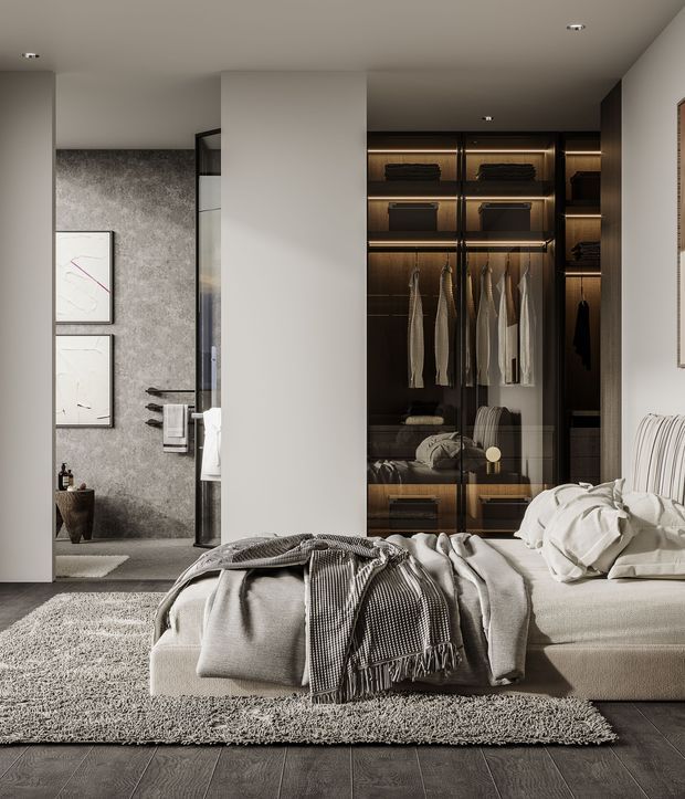 A refined contemporary bedroom in a neutral palette, featuring a low upholstered bed layered with soft white bedding and a textured throw. Full-height dark-framed glass wardrobe joinery with warm internal lighting forms a prominent feature wall, while a textured grey wall and minimalist framed artwork sit behind the bed area. Dark timber-look flooring and a large pale textured rug add contrast and warmth.