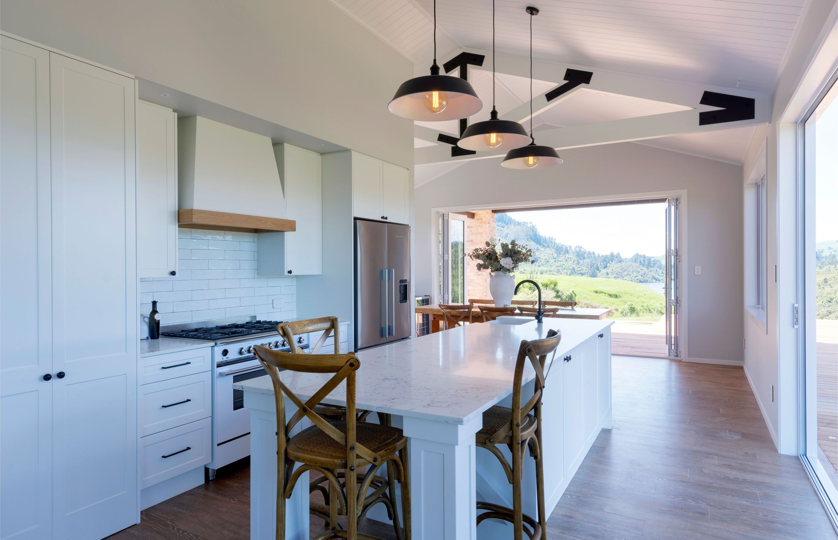 French Country-style kitchen where Arborform white satin cabinetry in the Ohope profile is complemented by Montrase pewter knobs and Delmore pewter cup handles. An island bench in Eurostone Constellation White from Pacific Stone is pristine beneath the vi