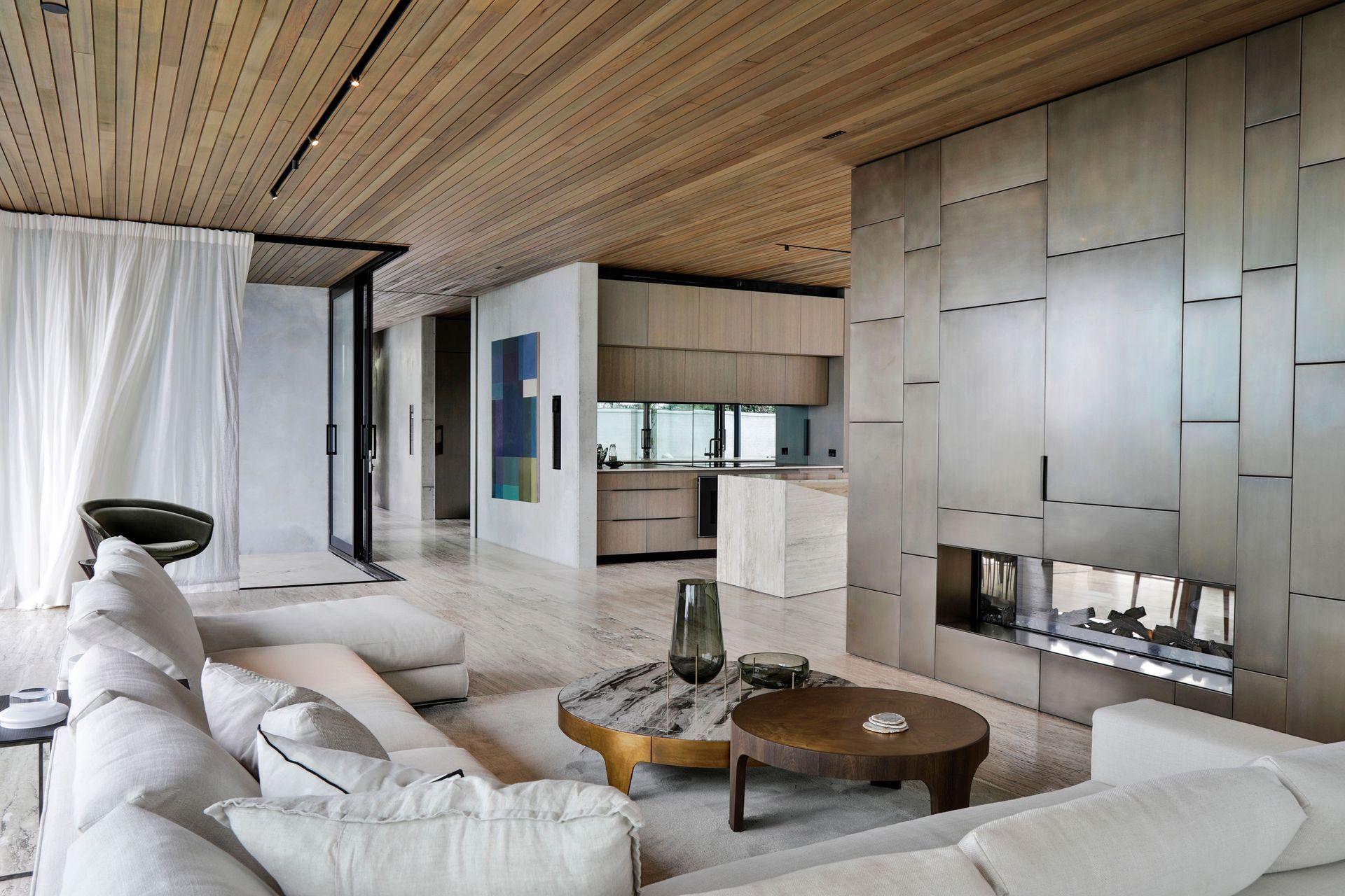 The colour palette in the downstairs living spaces takes in aged bronze on the fireplace, travertine floors, and serene floor-to-ceiling linen drapes.
