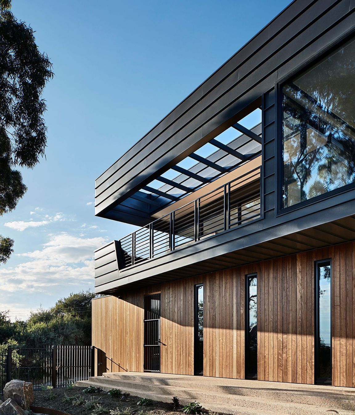 The solid timber cladding of the lower floor provides a base for the open air balcony above.