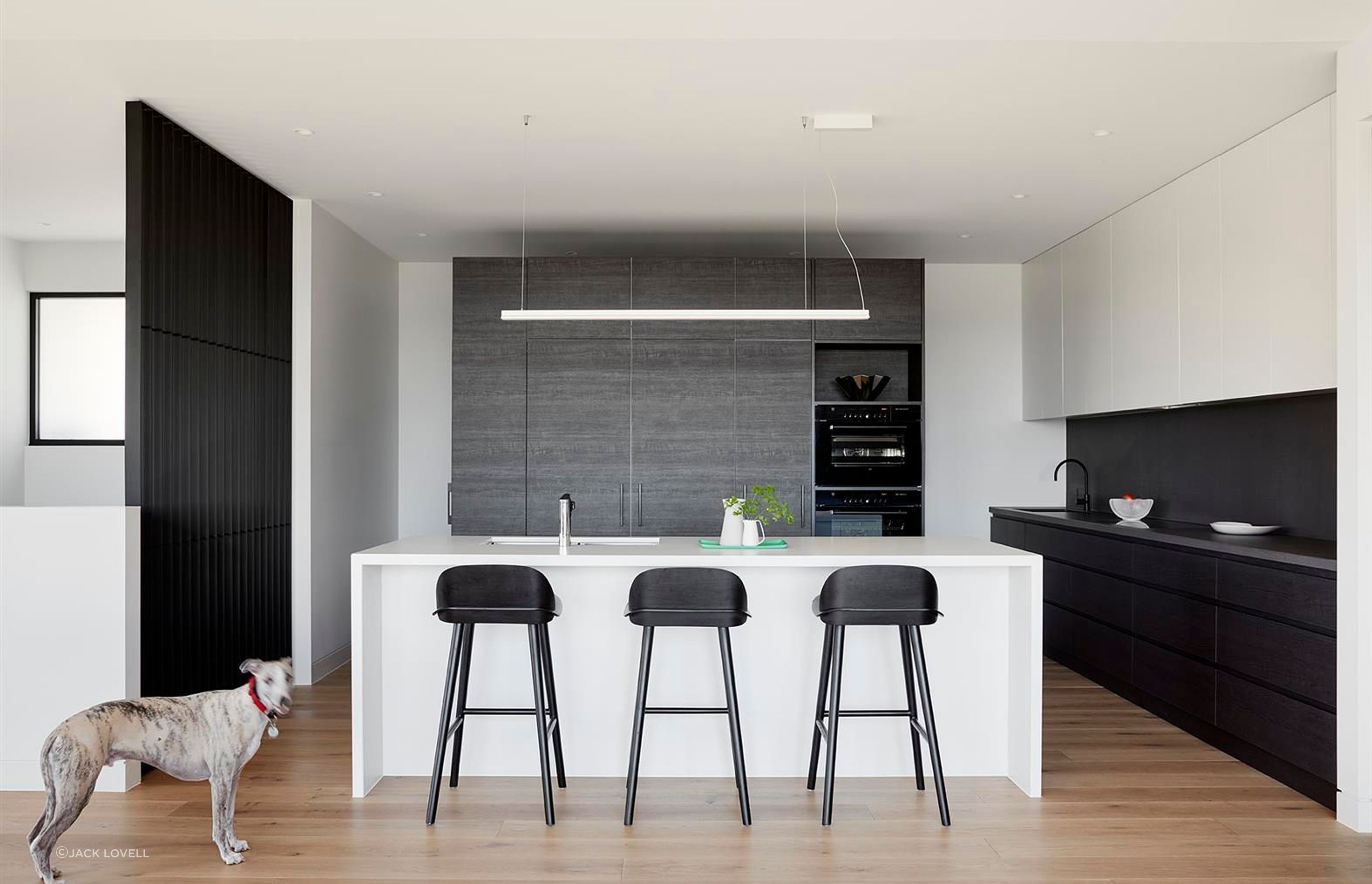 The Kitchen, as was the cellar, was central to the owner’s passion for food and wine. A dark timber veneer cabinetry ‘island’ sits behind the island bench and conceals a generous walk in pantry and storage area behind. Integrated fridges, and dark glass appliances allow this element to recede as a backdrop the bright white island bench.