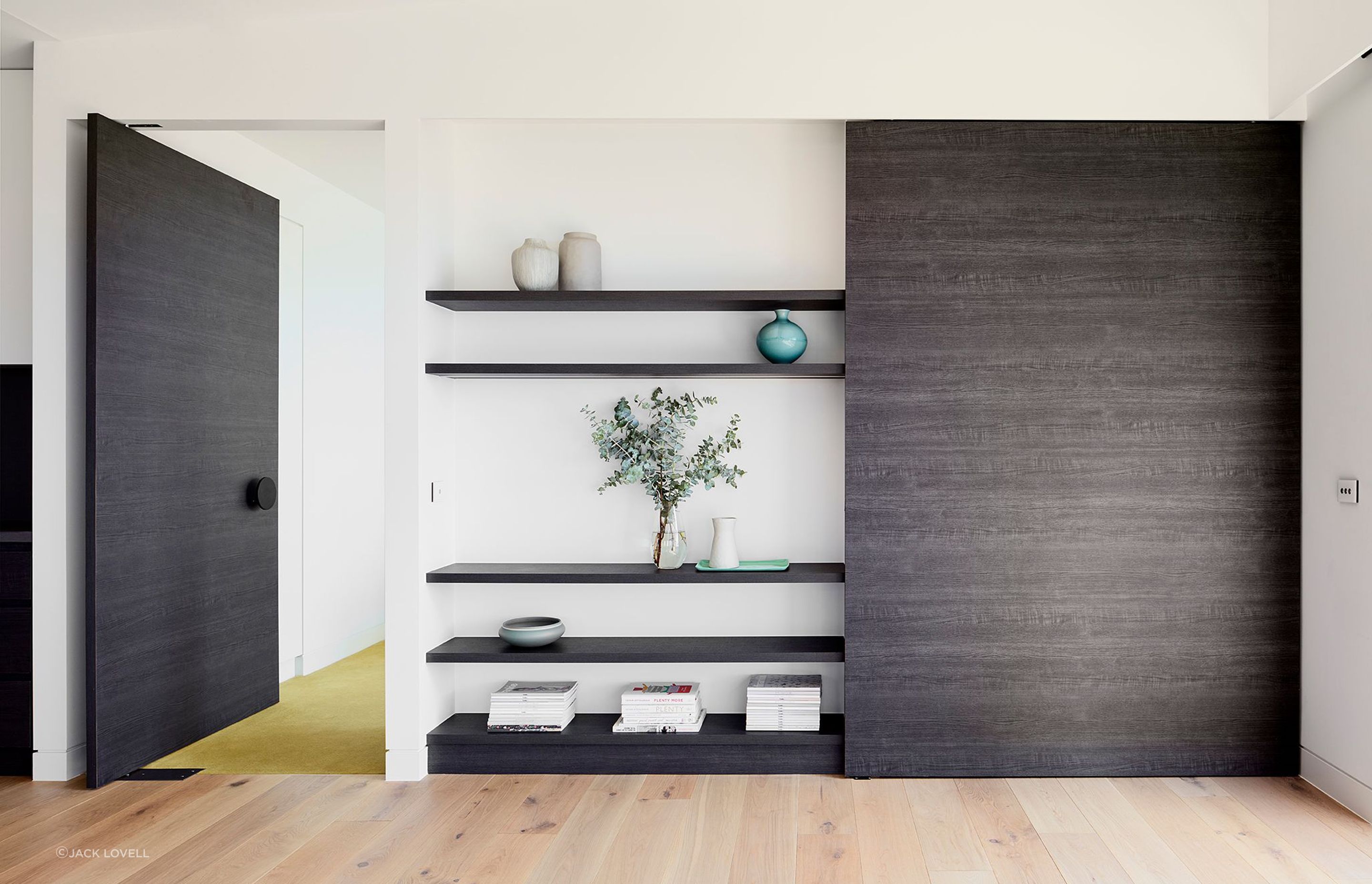 The dark veneer continues across the end wall of the Dining Room incorporating a large pivot door to the Master Suite and a concealed study nook – the green carpet of the bedroom echoing the cellar below.