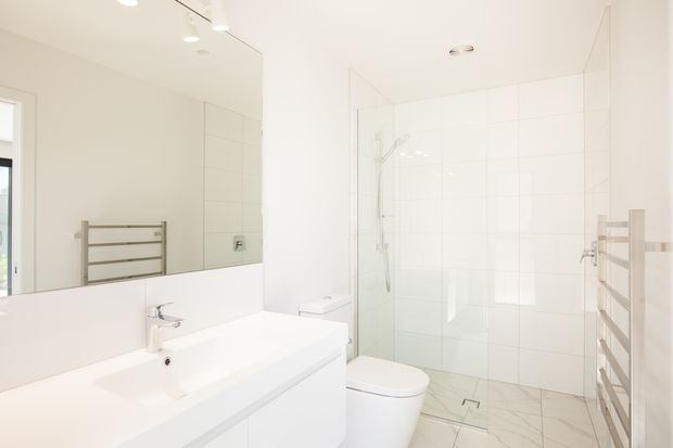 Bright contemporary white bathroom with a floating vanity, integrated basin, large wall mirror, wall-hung toilet, glass-enclosed walk-in shower, white tiled walls, pale marble-look floor tiles, and a wall-mounted heated towel rail.