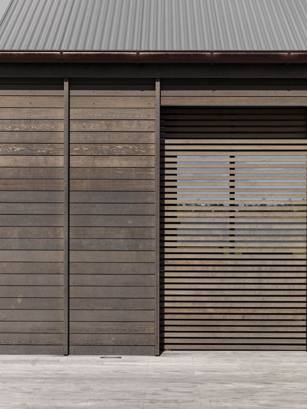 Close-up exterior view of a contemporary timber-clad facade with horizontal weathered wood boards, dark vertical framing, a corrugated metal roof, and a large horizontal slatted screen opening. Pale concrete paving is visible at the base, with limited views through the screen to the exterior beyond.
