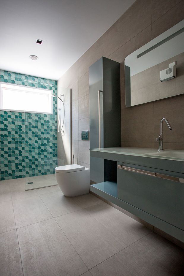Contemporary bathroom with a wall-hung vanity, integrated basin and chrome tapware, large rectangular mirror, concealed toilet, and walk-in shower. The room combines large taupe-grey wall and floor tiles with a striking teal and aqua scallop-pattern feature tile wall.