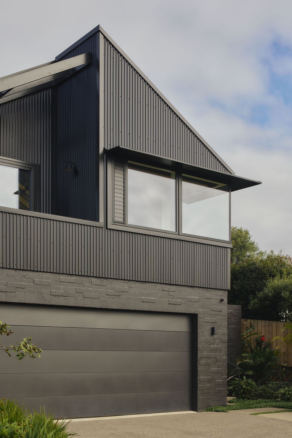 The front elevation combines black corrugated metal cladding with finely detailed aluminium joinery and a distinctive metal eyebrow, creating a refined contemporary coastal façade.