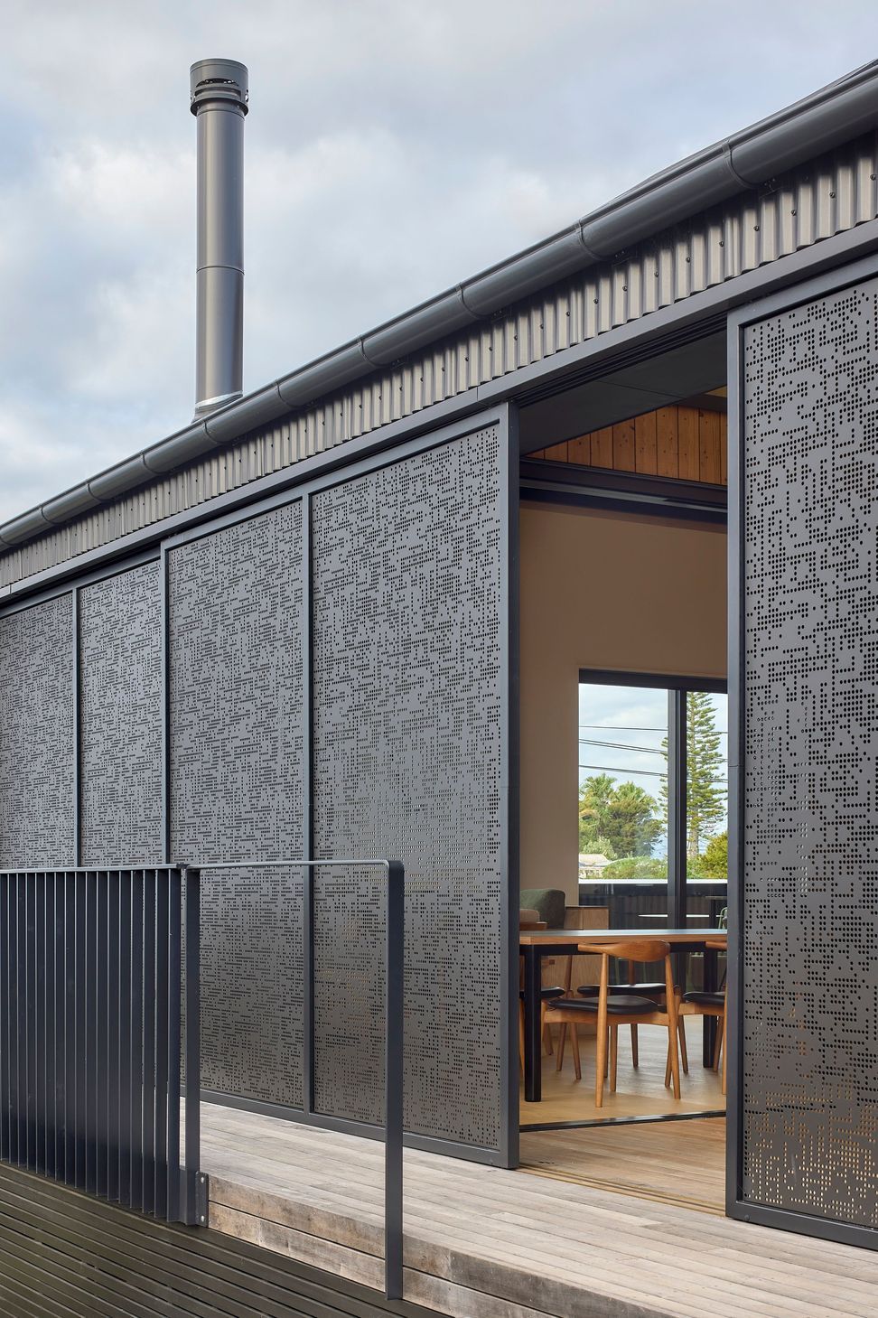 Operable perforated metal screens slide open to reveal the sheltered internal courtyard. The enclosed outdoor room forms the heart of the home, connecting directly to the dining space beyond.