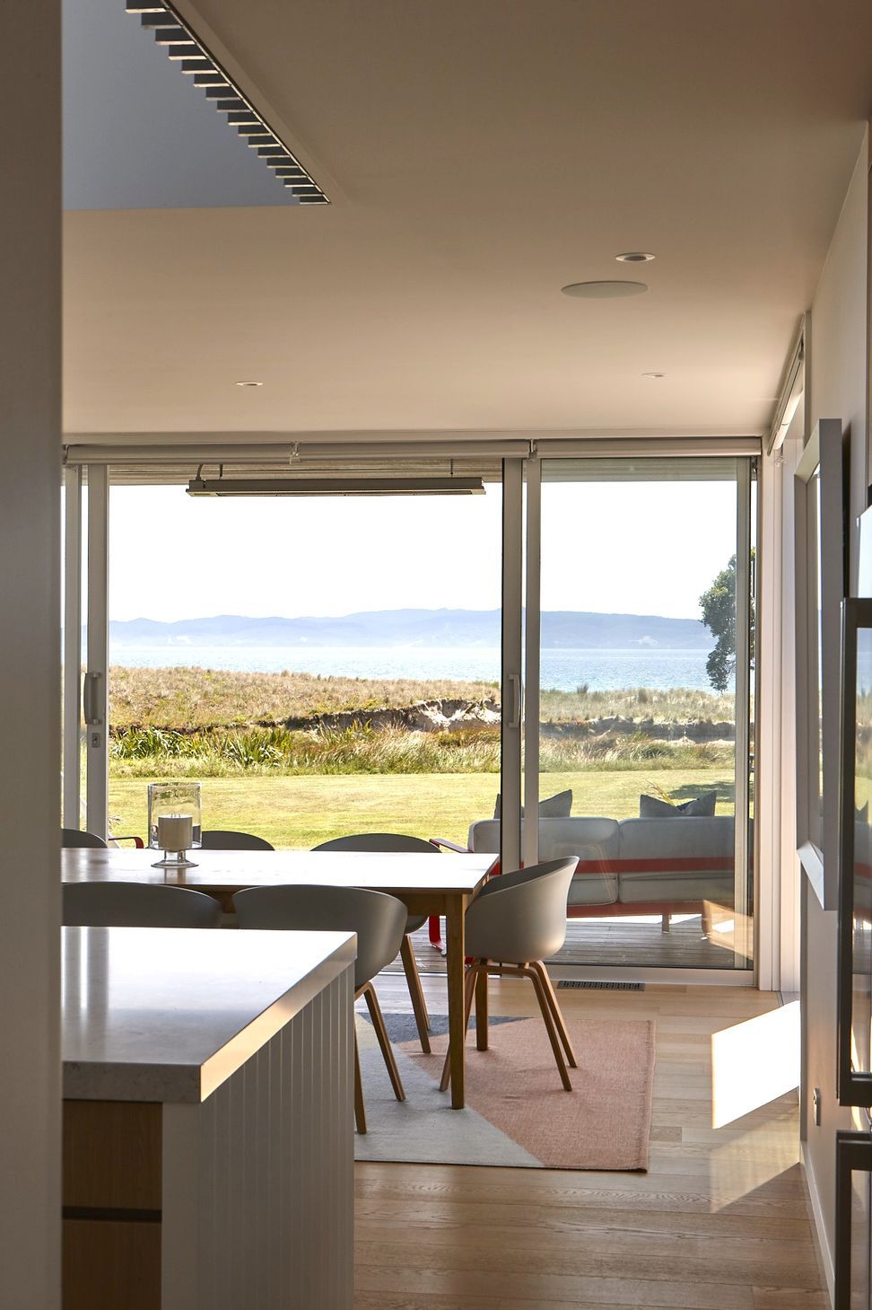 From the entrance hall, carefully framed views lead directly through the home towards the open-plan living spaces and the ocean beyond. The architecture uses transparency and natural light to strengthen the connection to the landscape.