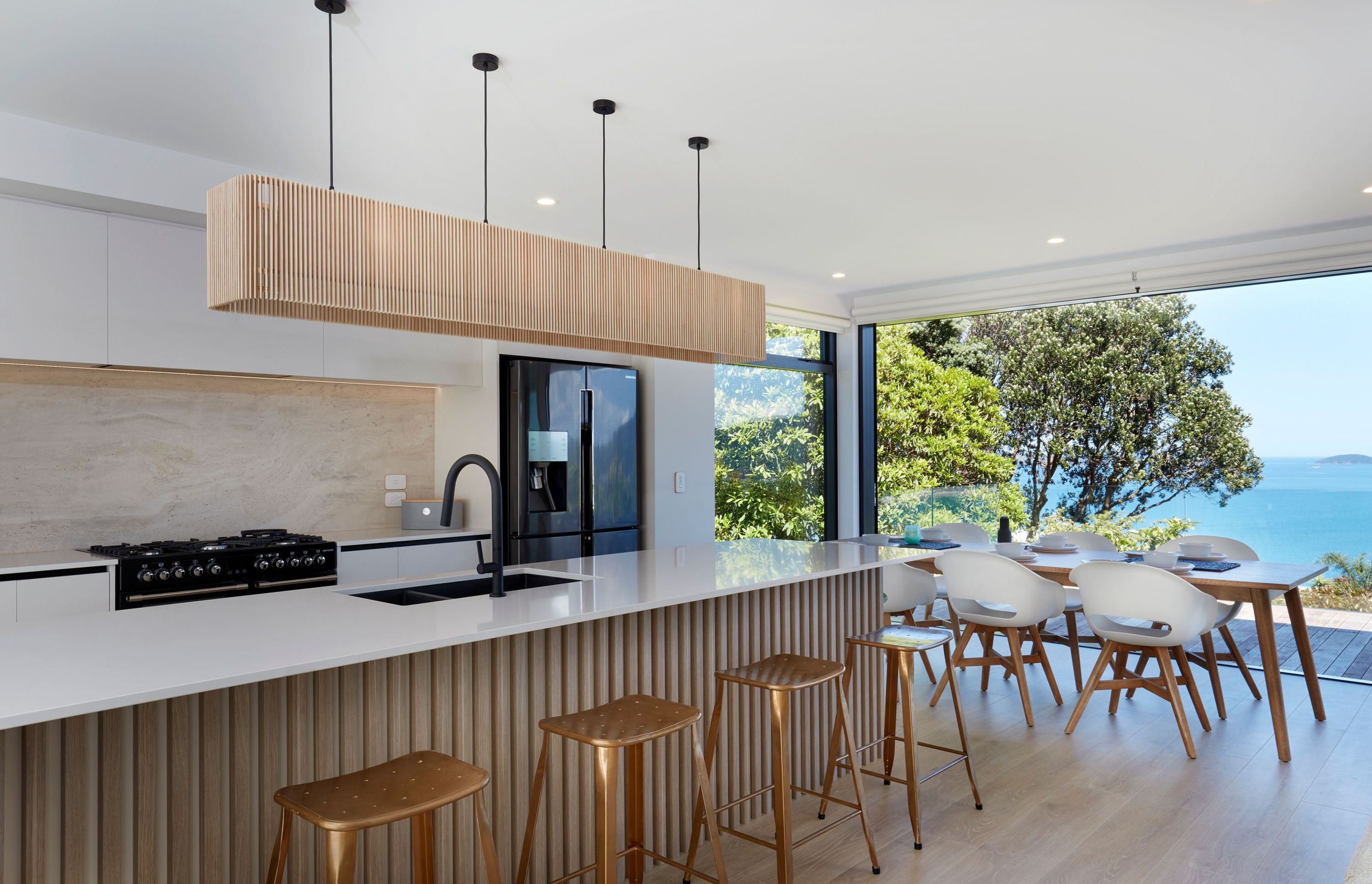 The team at Hostess Kitchens in the Waikato helped the owners with the design of their kitchen, which features a beautifully minimal Greens Luxe pull-out sink mixer. A Frankie Oak dining table from A&amp;C Homestore allows a primo view across the ocean du