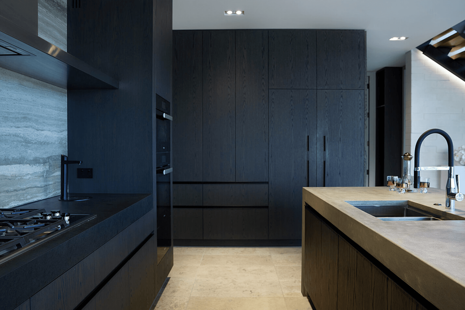 The dark kitchen cabinetry juxtaposes against the sandy-coloured floor and concrete island.