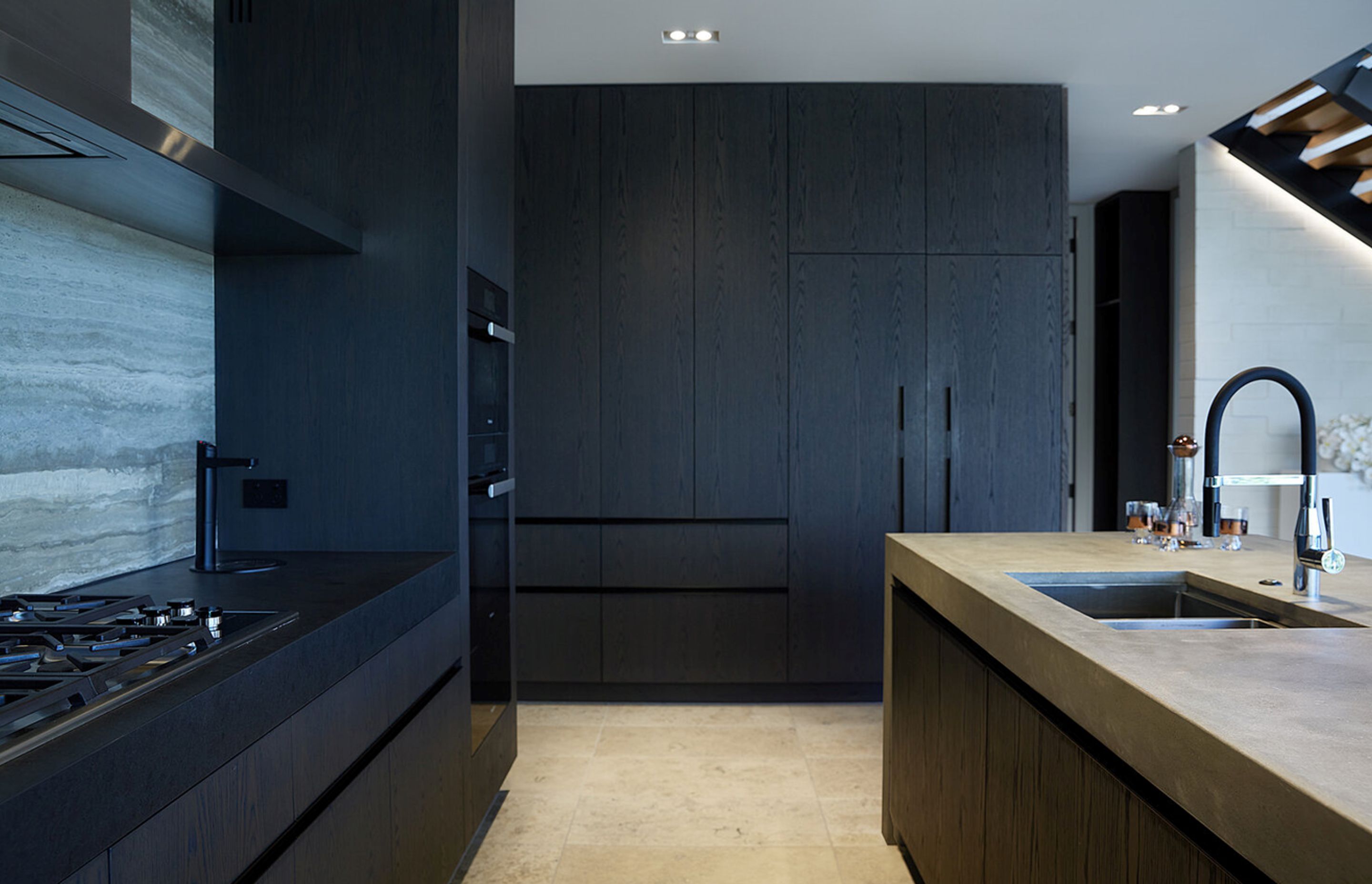 The dark kitchen cabinetry juxtaposes against the sandy-coloured floor and concrete island.