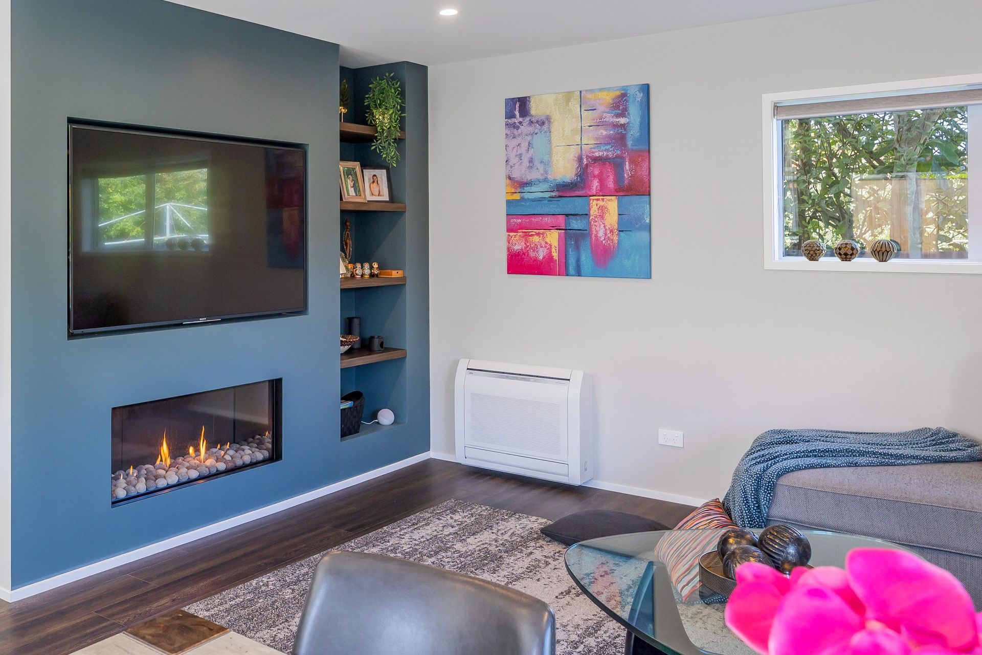 The Feature wall separating the staircase from the Living Room is a wall that was specifically built to house the TV and the Fireplace, as well as provide a recessed shelf where the client's can display photographs and personal belongings.  This Living Room being part of the open plan kitchen / dining / living with access to the deck and outdoor dining, serves as a central gathering space for family members and guests to socialize, relax, and spend quality time together. It is the space where they can engage in conversations, watch movies or TV shows, play games, and enjoy various forms of entertainment. This living room acts as the focal point for hosting guests and creating a welcoming atmosphere.