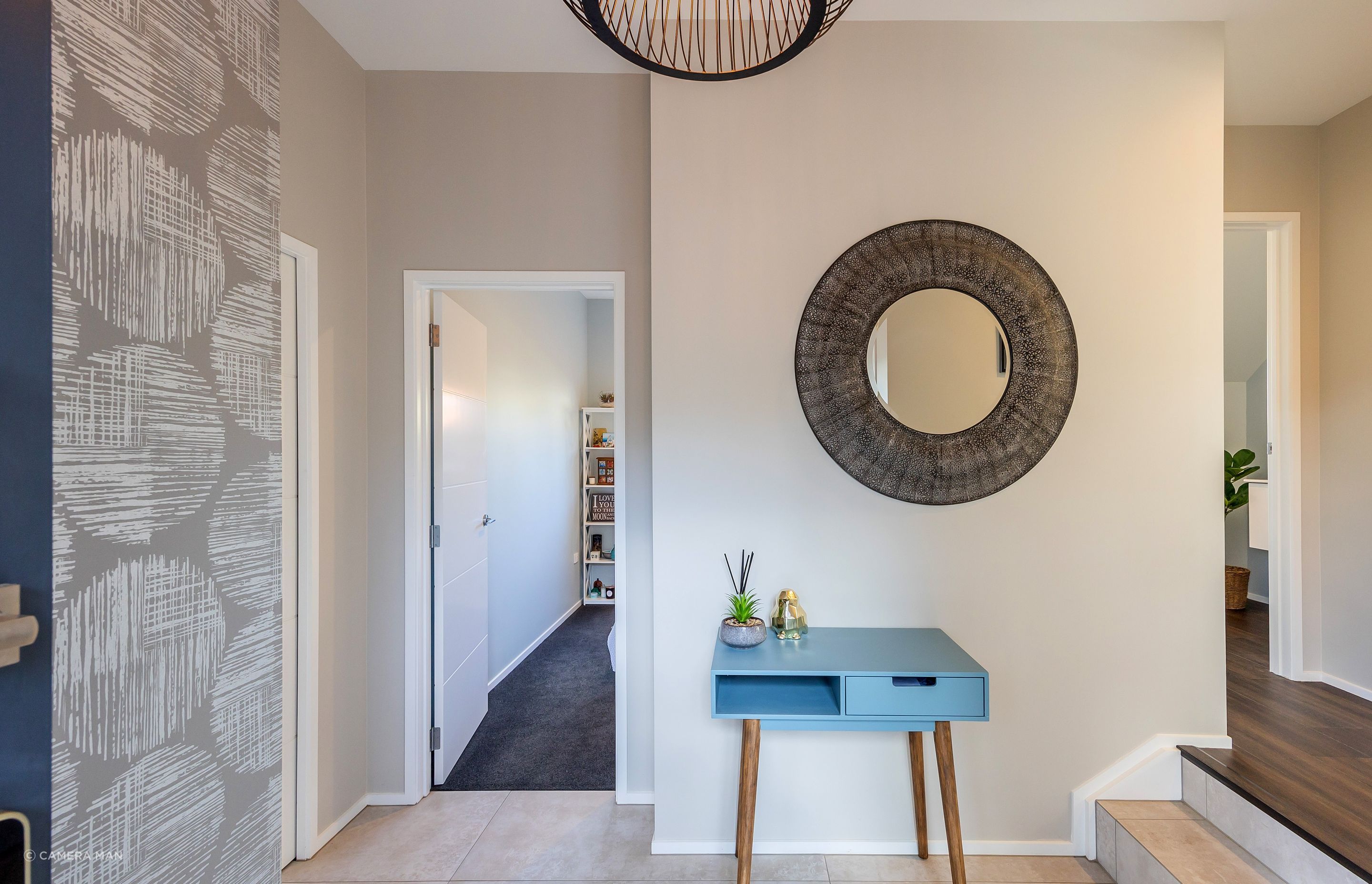 The entry foyer sets the tone for the rest of the home. It creates an initial impression and establishes the overall ambiance and style. We included an in-built closet to ensure that the space can remain cutter free, providing a designated space for belongings. We wanted to create a visual impact, by using a feature wallpaper and feature pendant light. The client found the mirror, which really sets the aesthetic tone for the rest of the interior. Aspiring Walls Focus Collection Spots &amp; Stripes Page 33 Pattern 30550-1 to feature wall Resene Alabaster to architraves &amp; skirting Resene Triple White Pointer to all walls and ceiling Gravity Pearl Porcelain Tile 600x1200 Matt to entry floor with grout colour Mapei Medium Grey 112 (Tile layout: straight stack)