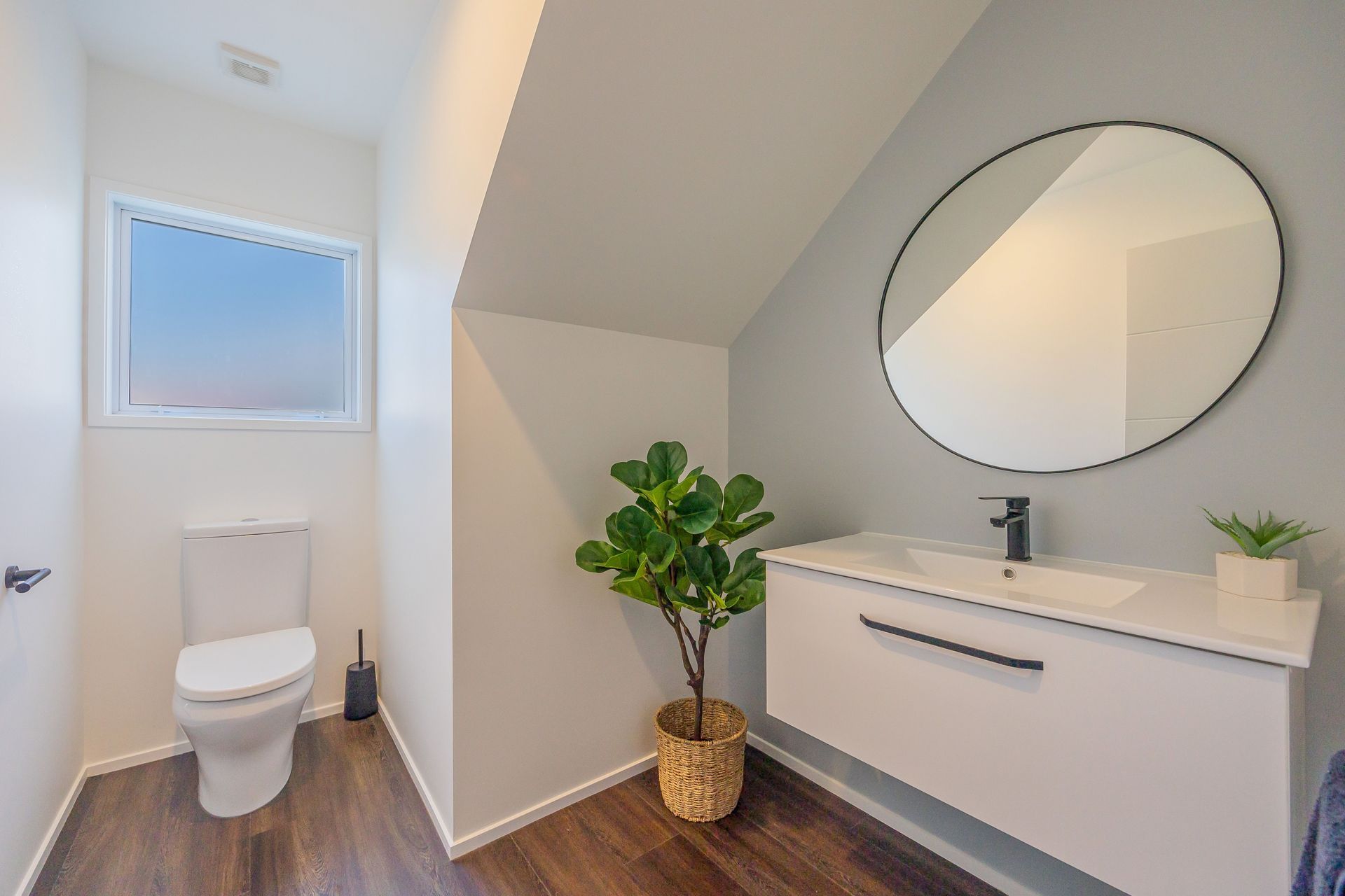This Powder Room has the main flooring material run into it to ensure a cohesive progression from the spaces. We used the area under the stairs for the vanity and accessorized with a large mirror. Resene Alabaster to ceiling, architraves &amp; skirting as well as all walls apart from feature wall; Resene Half Emerge to feature wall; Moduleo Transform Falcon Wood 28890 to floor