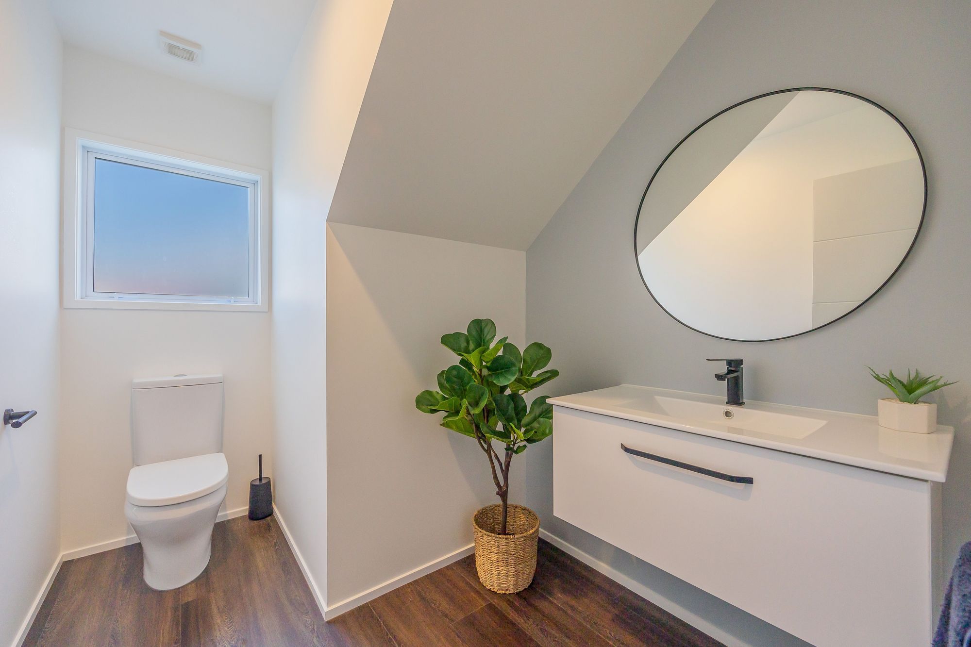This Powder Room has the main flooring material run into it to ensure a cohesive progression from the spaces. We used the area under the stairs for the vanity and accessorized with a large mirror. Resene Alabaster to ceiling, architraves & skirting as well as all walls apart from feature wall; Resene Half Emerge to feature wall; Moduleo Transform Falcon Wood 28890 to floor