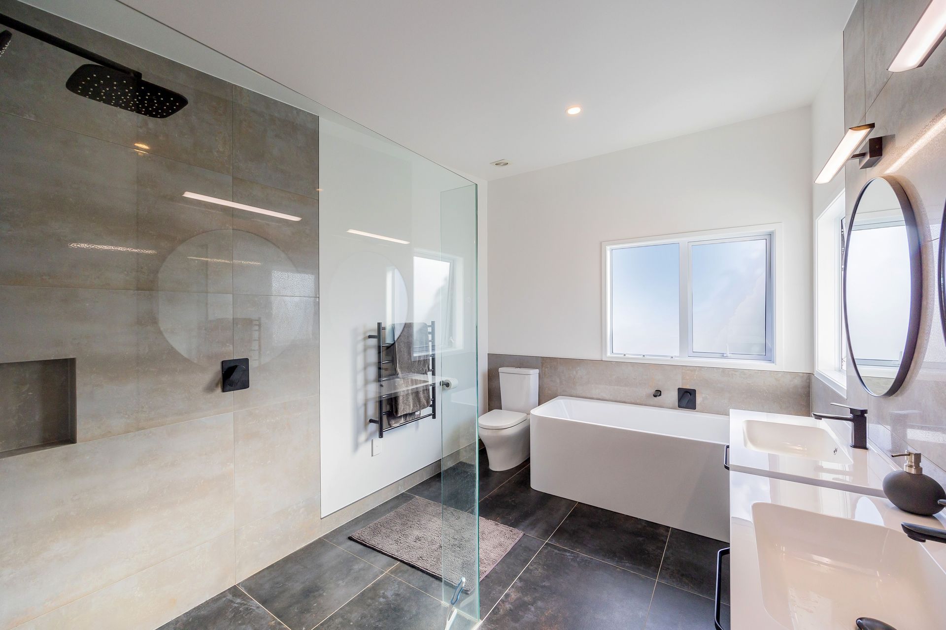 For the Master Bathroom we wanted to create a sophisticated and elegant atmosphere. To make the layout feel more spacious we used his and hers vanity cabinets both with circular mirrors over. The task lighting for grooming above the mirrors and ambient lighting for relaxation, enhances the functionality and mood of the room.
