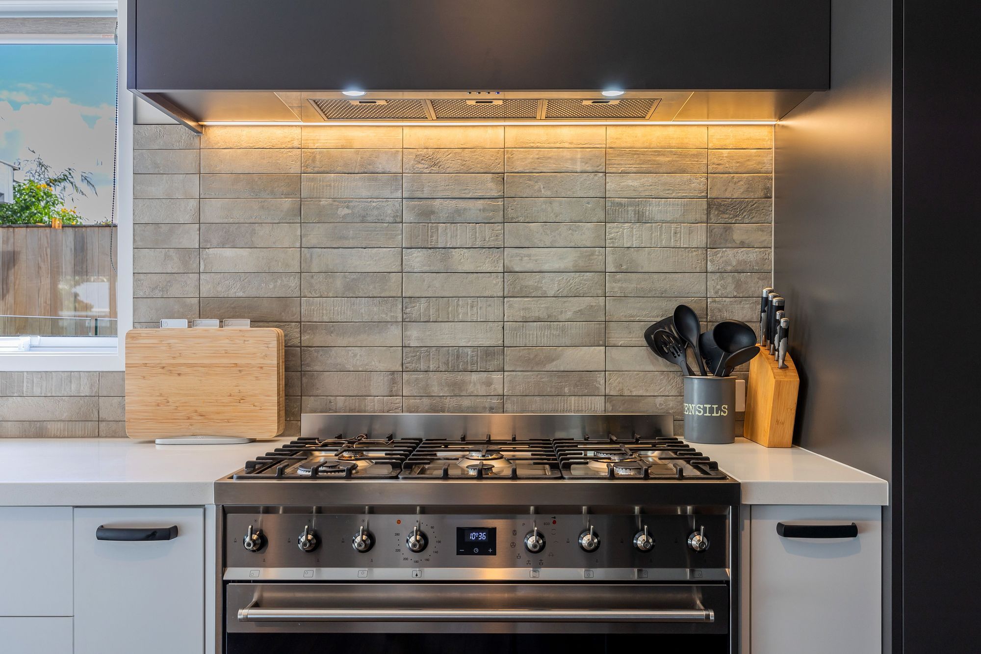 Eurostone Breeze Blanc to benchtop; Prime Melamine Ironsand to kitchen high wall & overhead cabinetry; Emil Ceramica Kotto Cenere Brick 60x250 to kitchen splashback (with grout colour Mapei Cement 113) Tile layout: straight stack; Tile set-out: from centre of wall; Prime Melamine White to kitchen under bench cabinetry; Resene Alabaster to ceiling, architraves & skirting; Resene Triple White Pointer to all walls; Moduleo Transform Falcon Wood 28890 196x1320 to floor