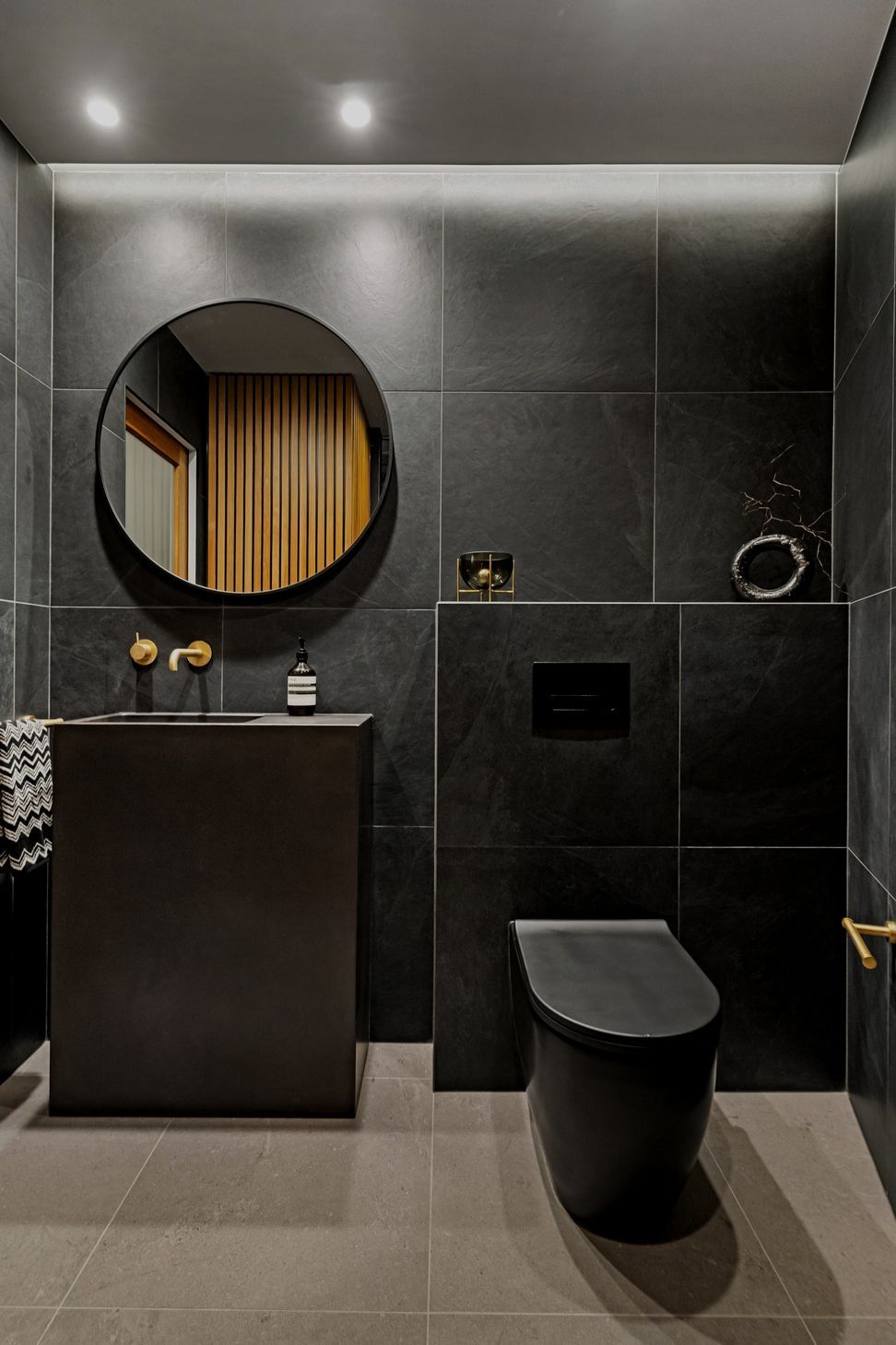 A refined color palette showcases aged brass Progetto tapware alongside elegant imported Italian black tiles and toilet, creating a sophisticated and cohesive aesthetic throughout the space.