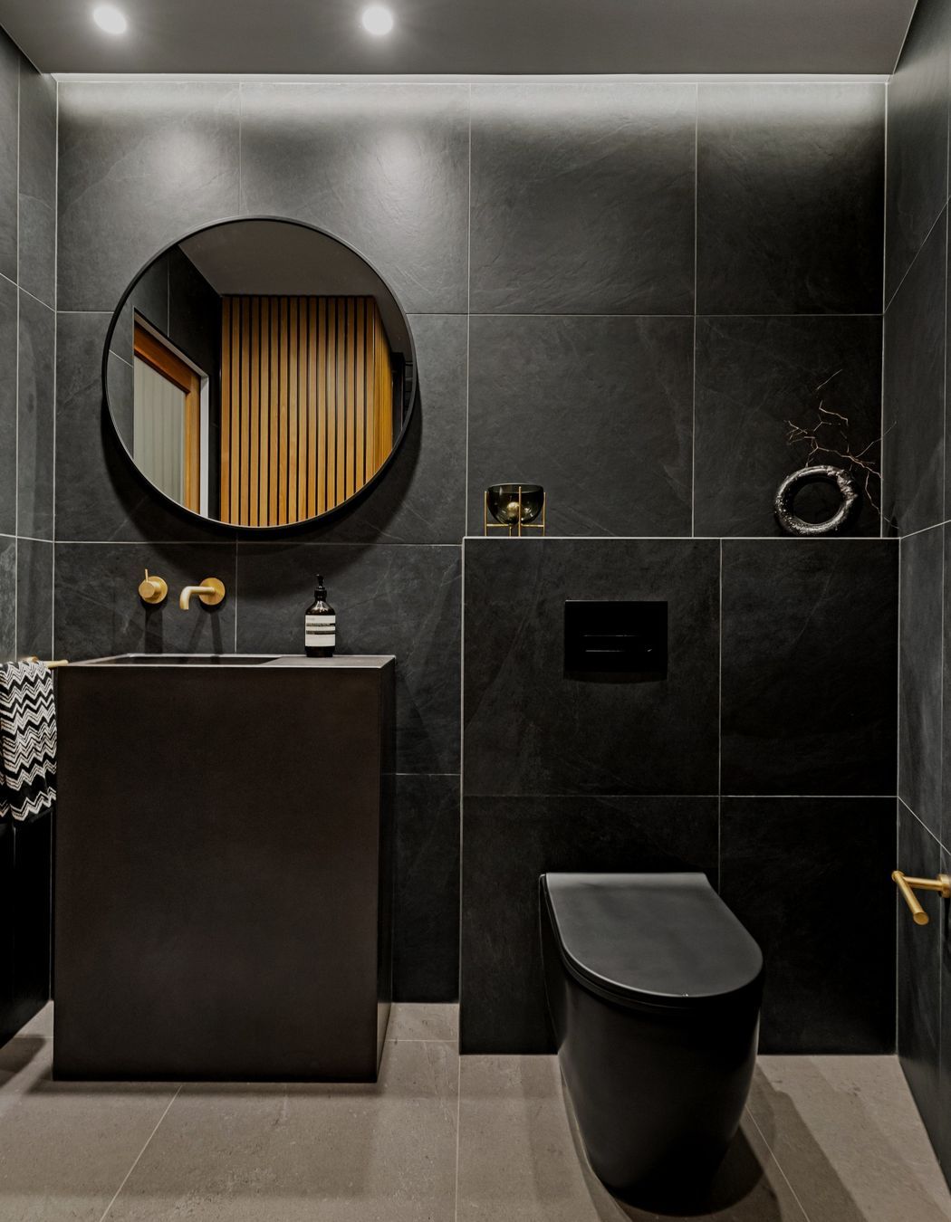 A refined color palette showcases aged brass Progetto tapware alongside elegant imported Italian black tiles and toilet, creating a sophisticated and cohesive aesthetic throughout the space.